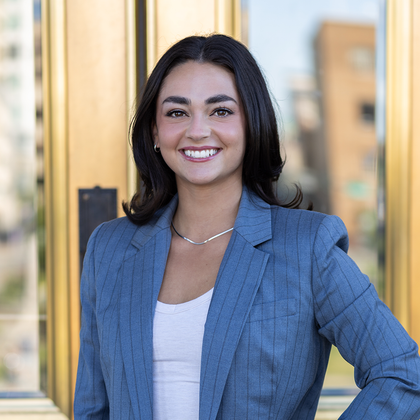 A woman in a blue suit is smiling and standing in front of a building.