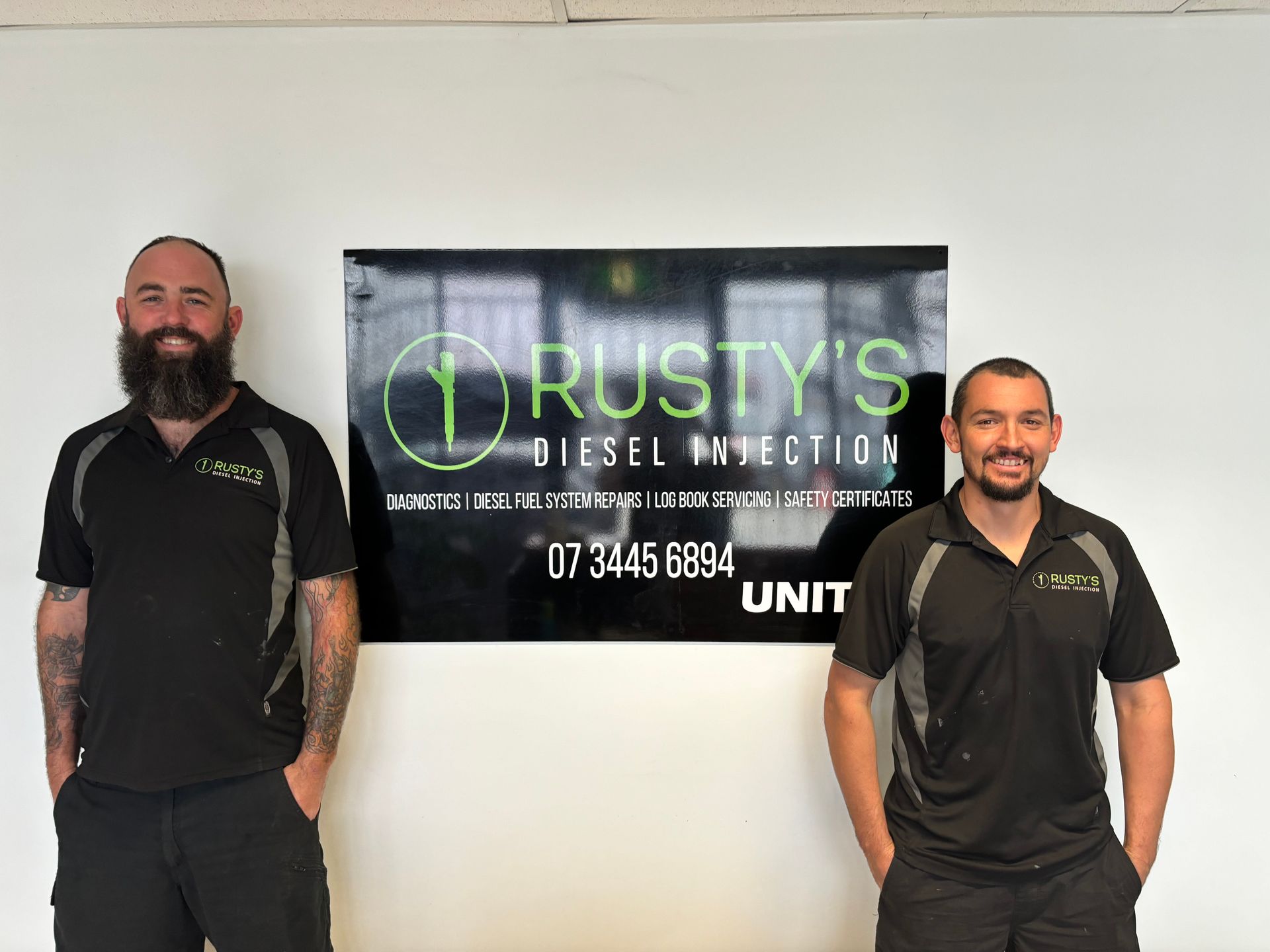 Two men are standing in front of a rusty 's diesel injection sign.