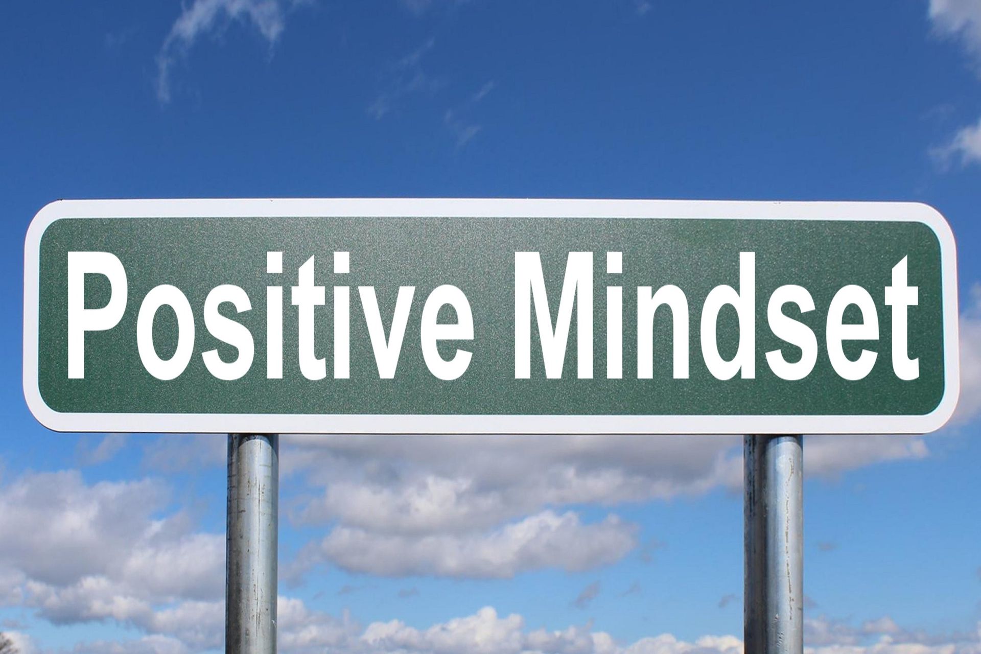 A road sign that says Positive Mindset on a sunny day with clouds in the background.