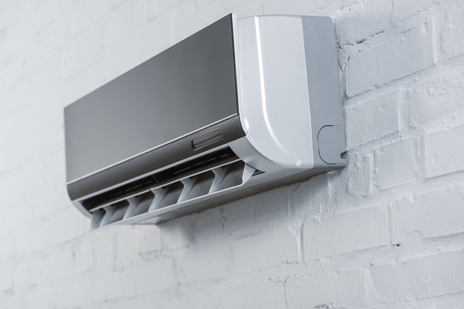Wall-mounted, split-system air conditioner, white and gray, on a white brick wall.