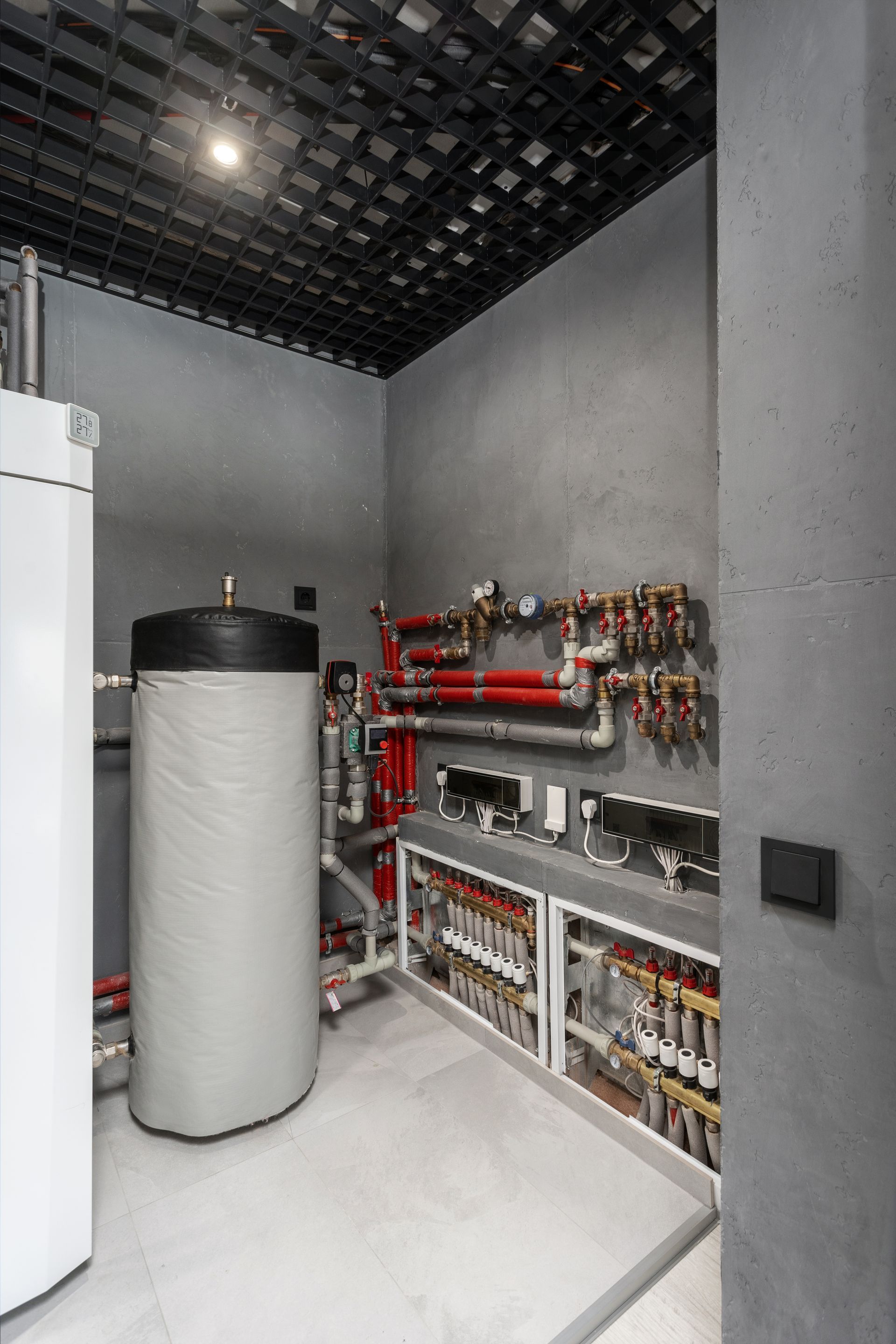 Utility room with gray walls, water heater, red pipes, and black ceiling.