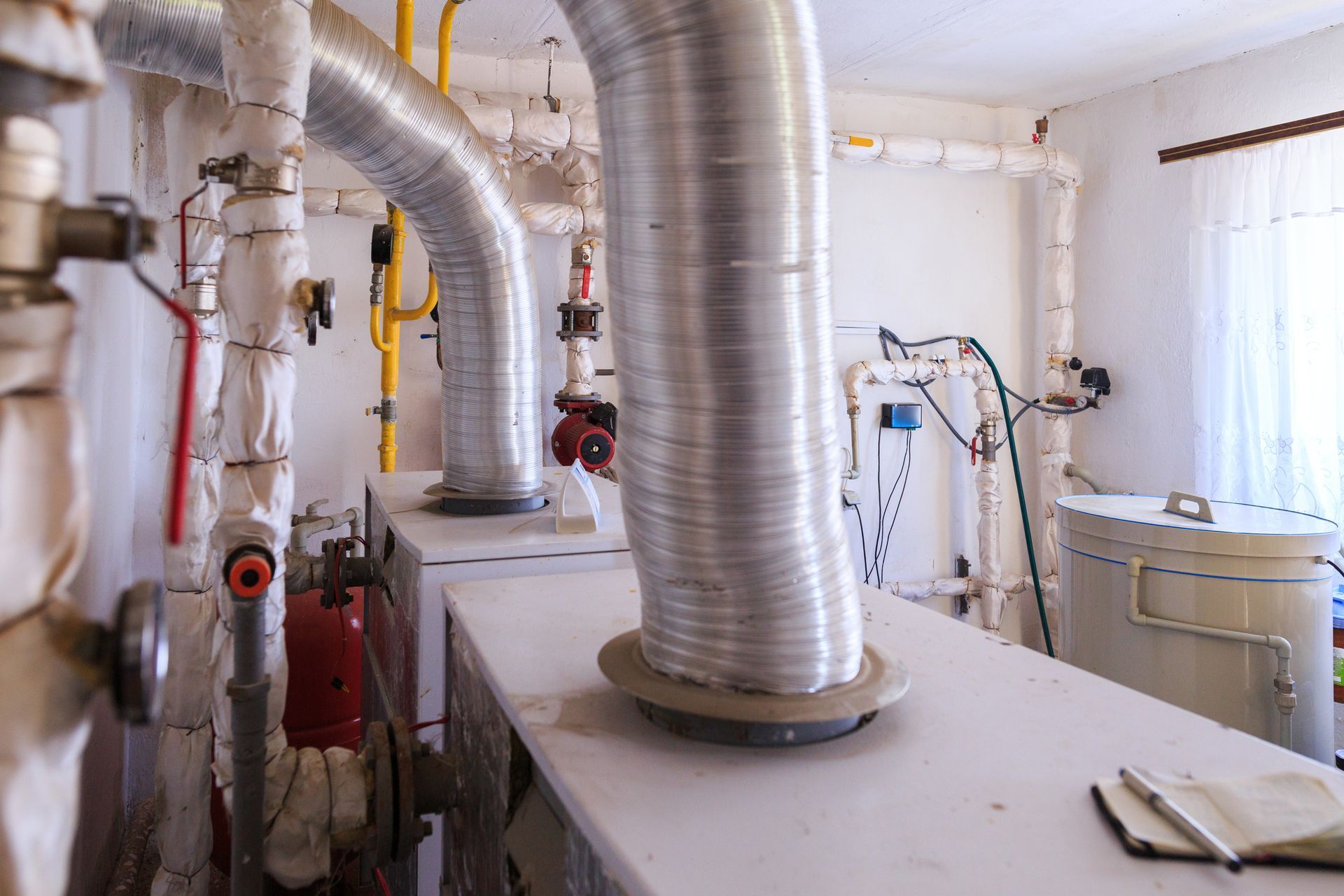 Interior of utility room with pipes, ducts, and machinery, white and silver tones.
