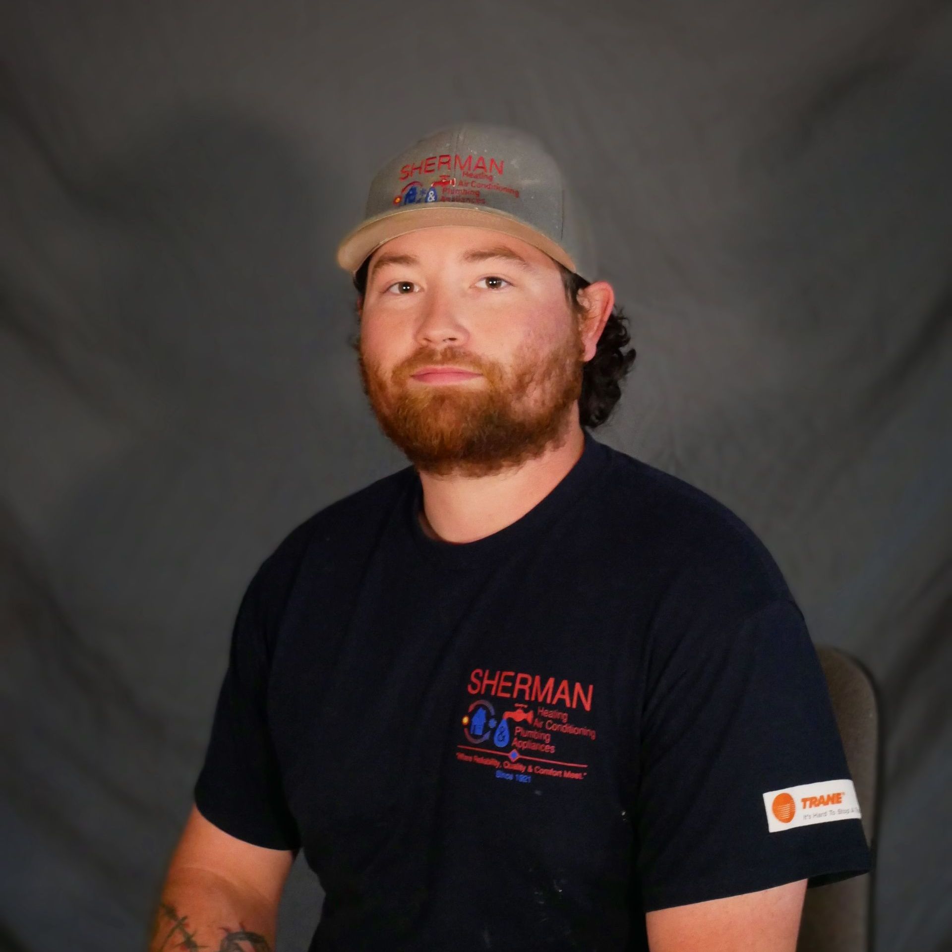 A man wearing a hat and a sherman shirt is sitting in a chair.