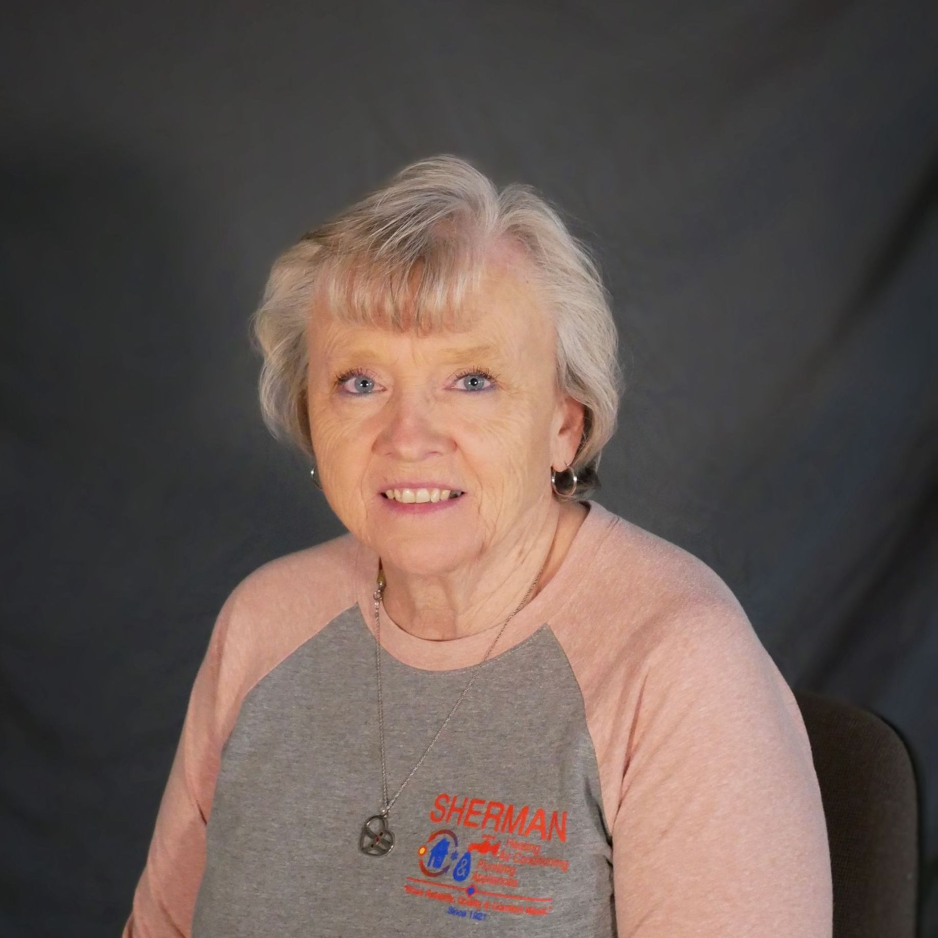 A woman wearing a gray shirt with the word sherman on it is smiling for the camera.