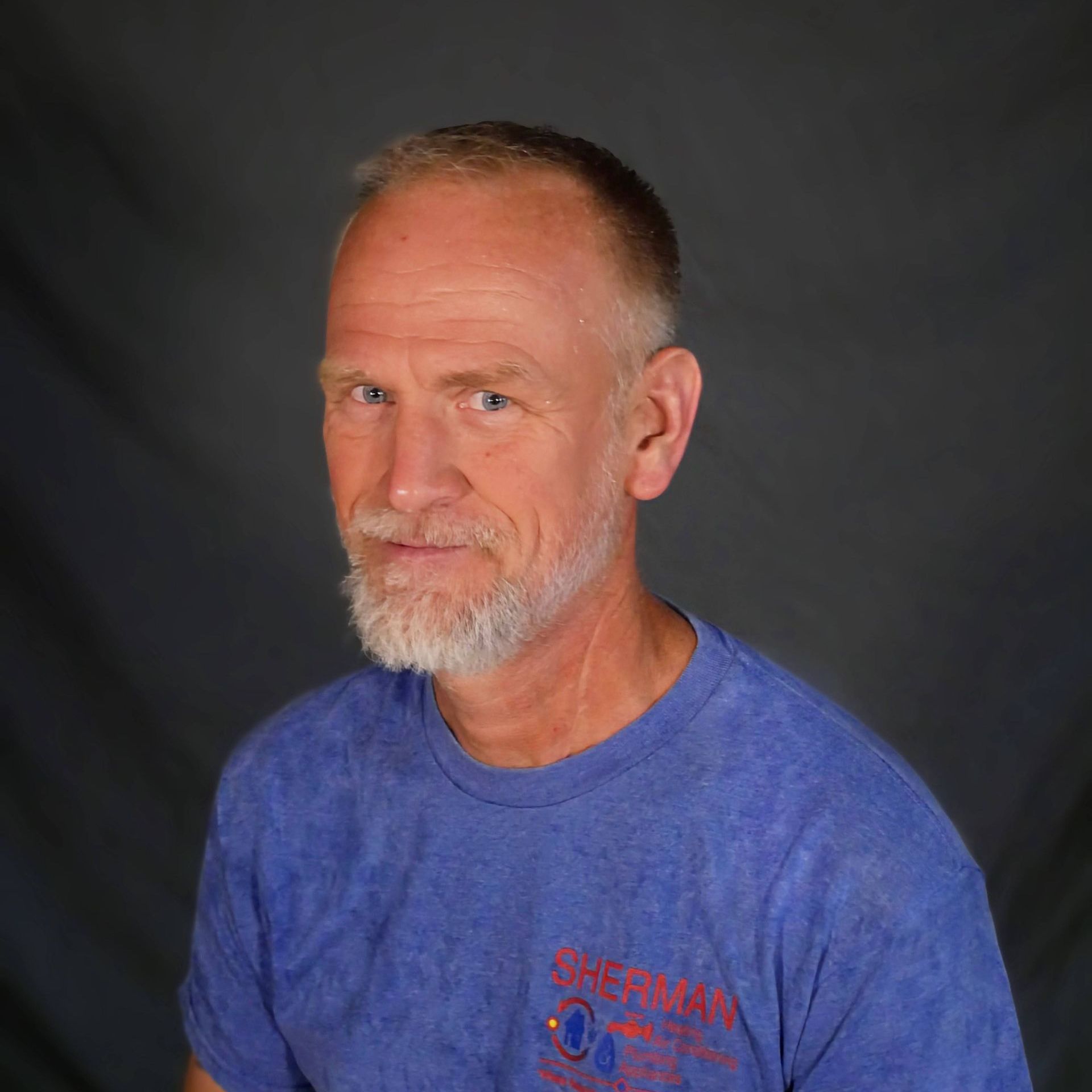 A man with a beard is wearing a blue t-shirt and looking at the camera.