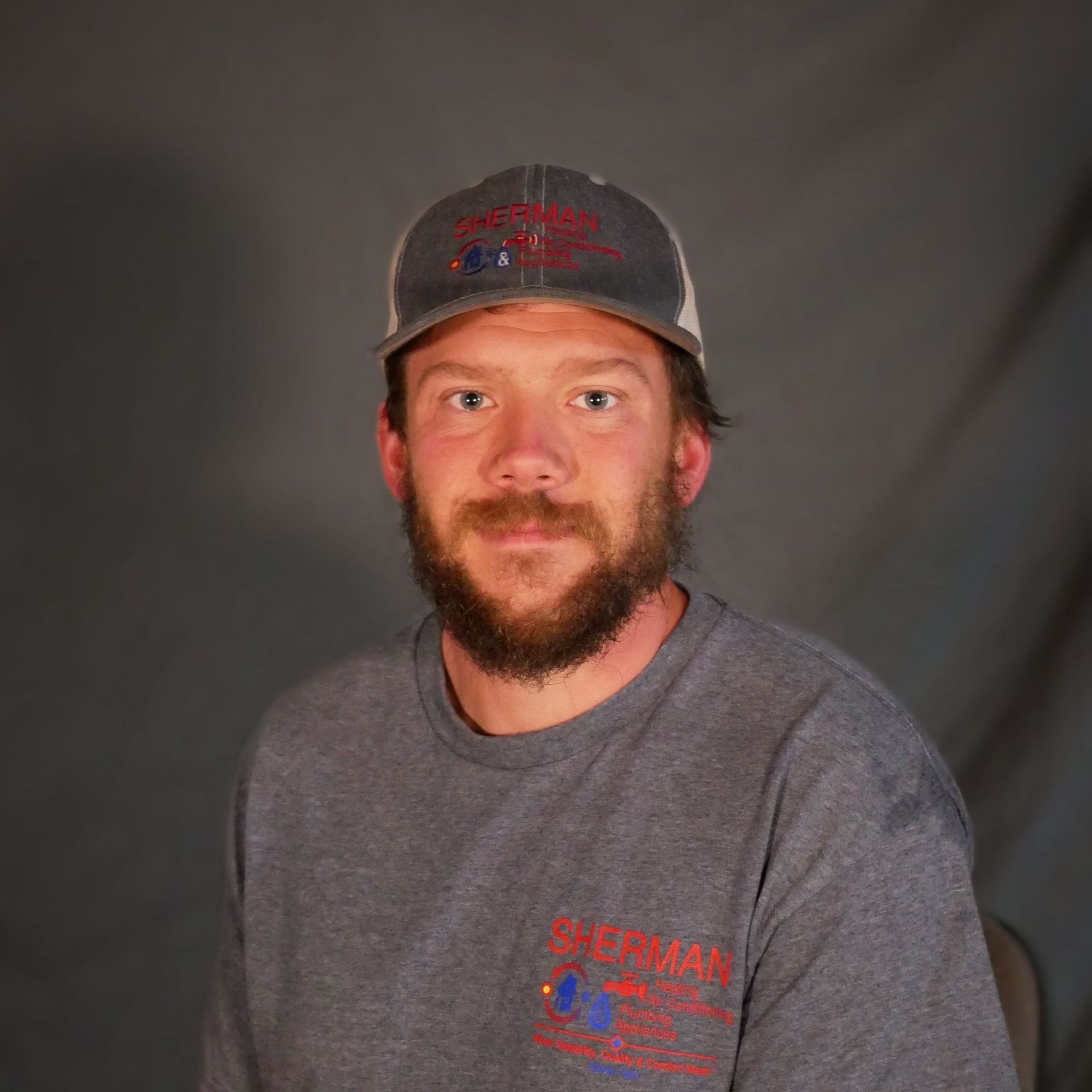 A man with a beard is wearing a hat and a gray t-shirt.