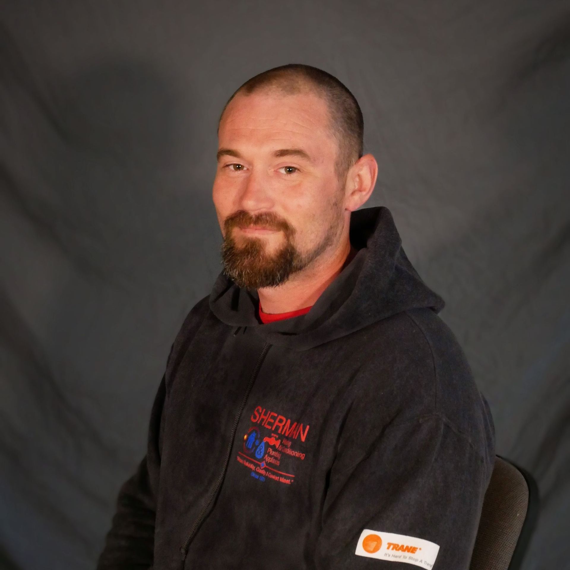 A man with a beard wearing a black hoodie is sitting in a chair.