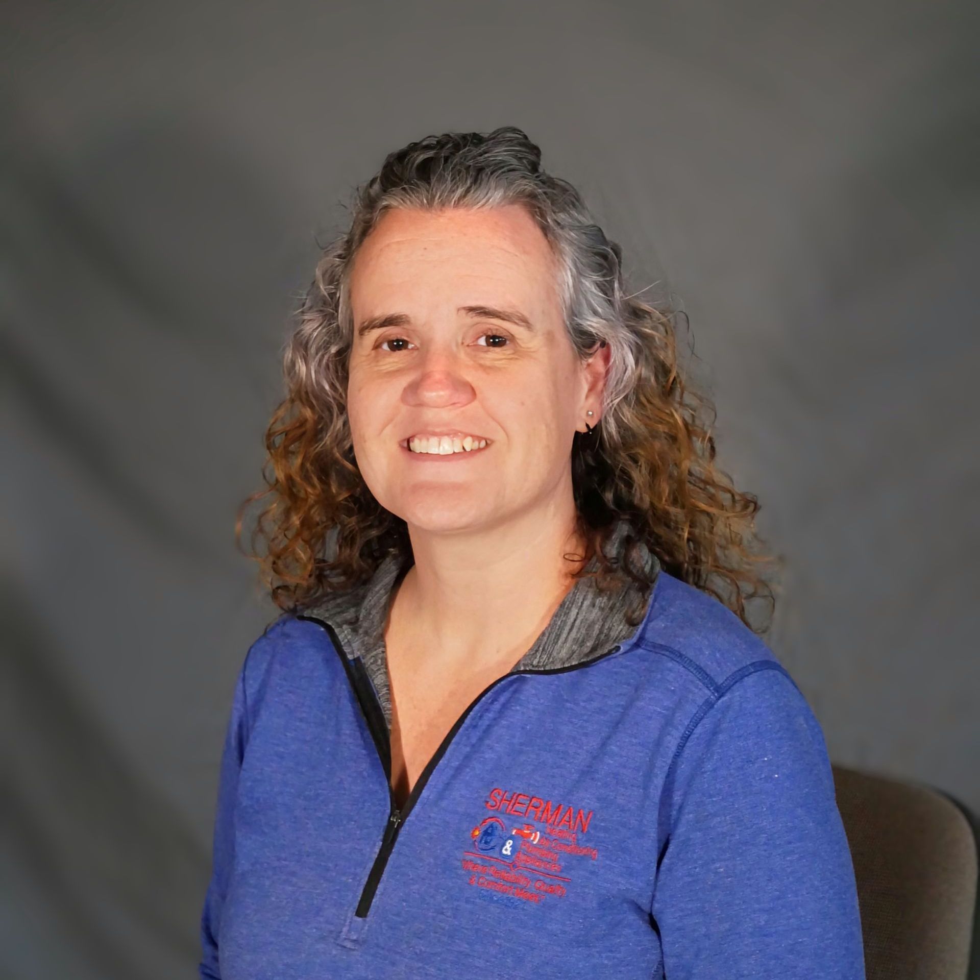 A woman with curly hair is wearing a blue sweater and smiling for the camera.