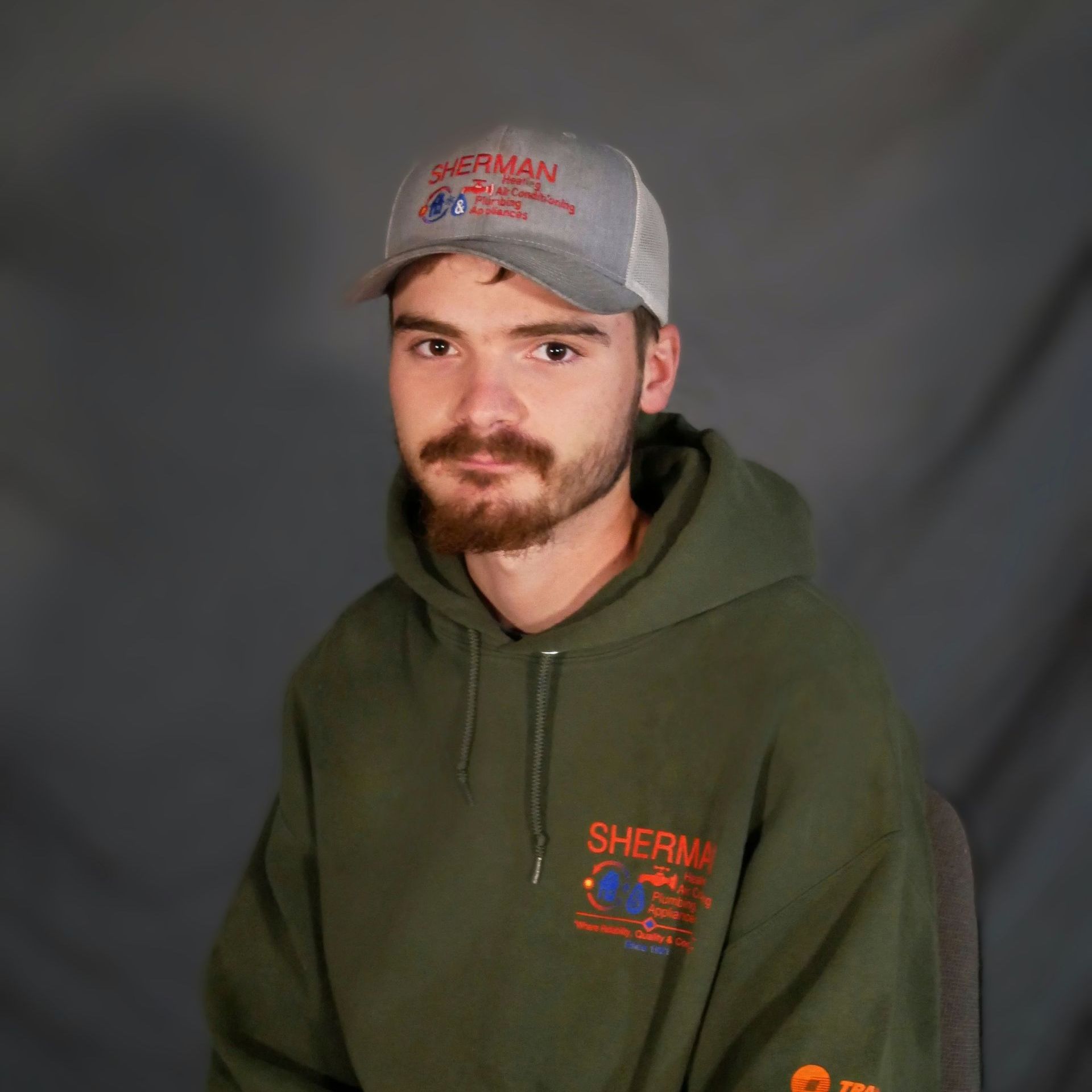 A man wearing a hat and a hoodie is sitting in a chair.