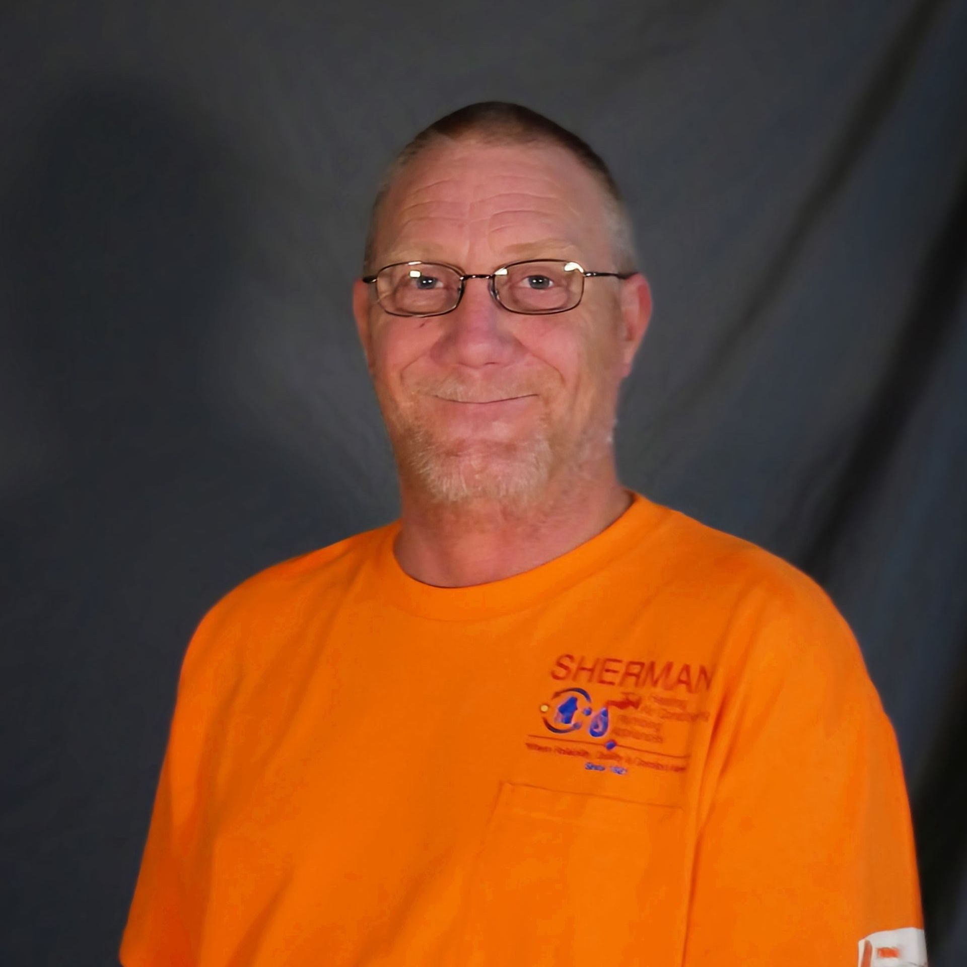 A man wearing glasses and an orange shirt with the word sherman on it