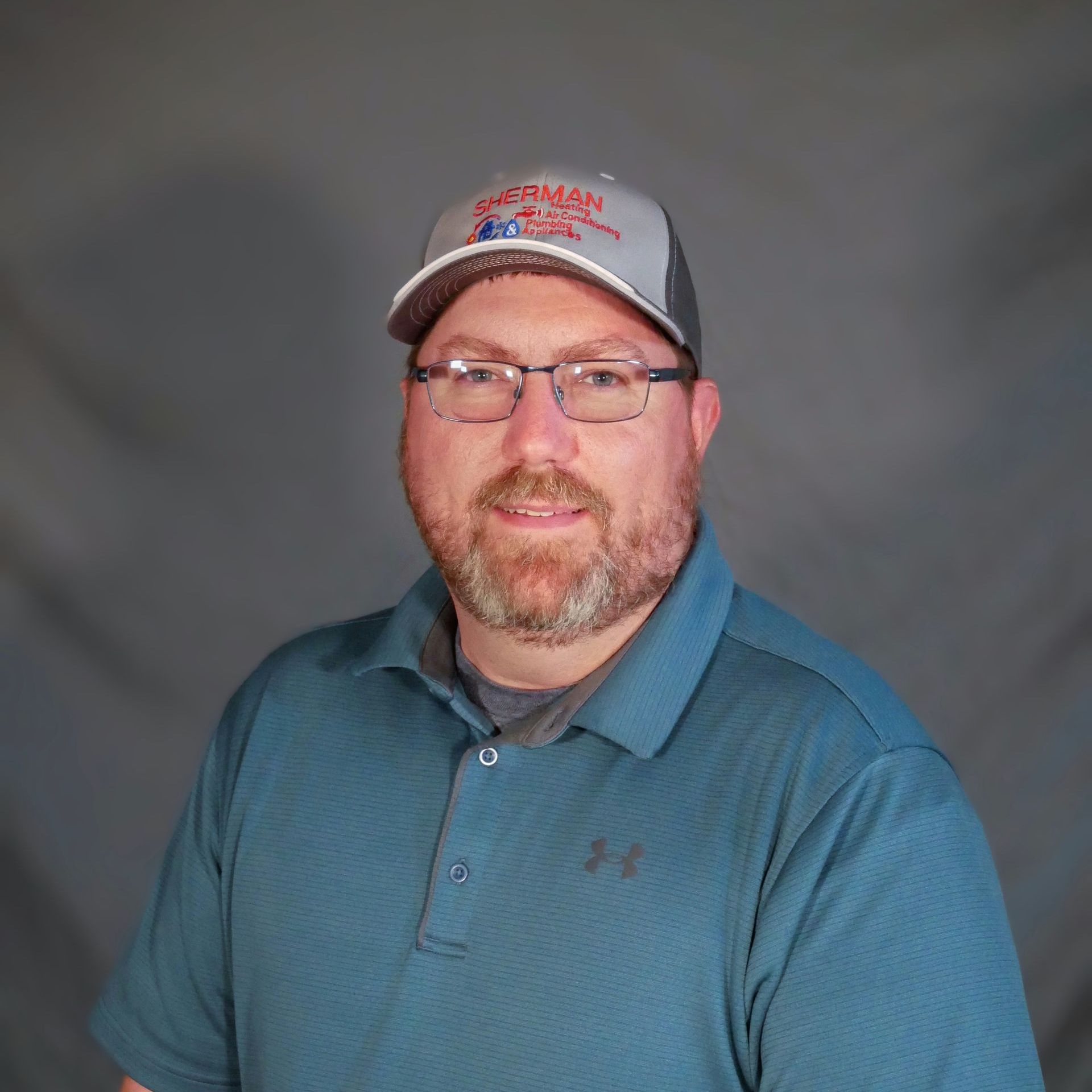 A man with a beard and glasses is wearing a hat and a blue shirt.