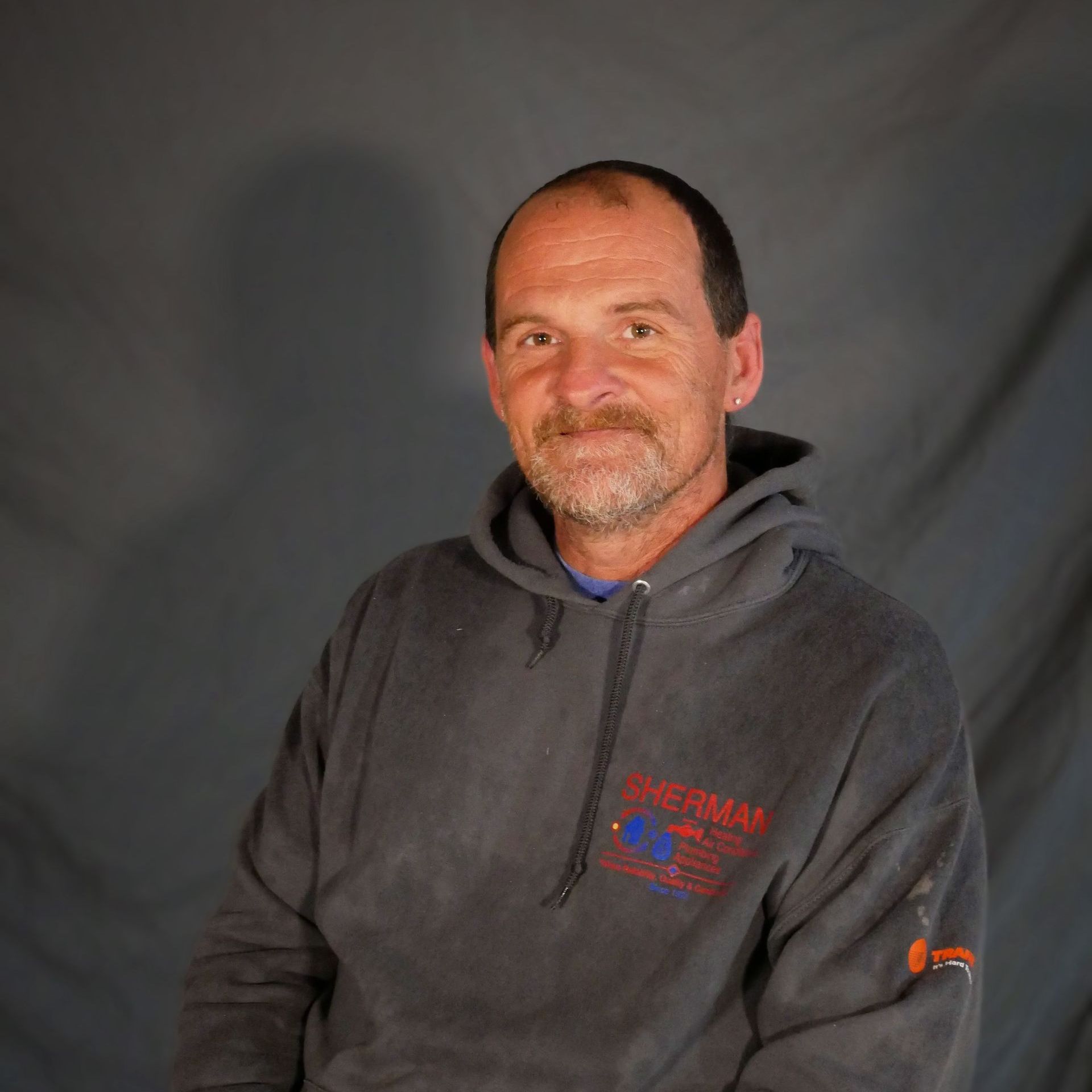 A man with a beard is wearing a gray hoodie.