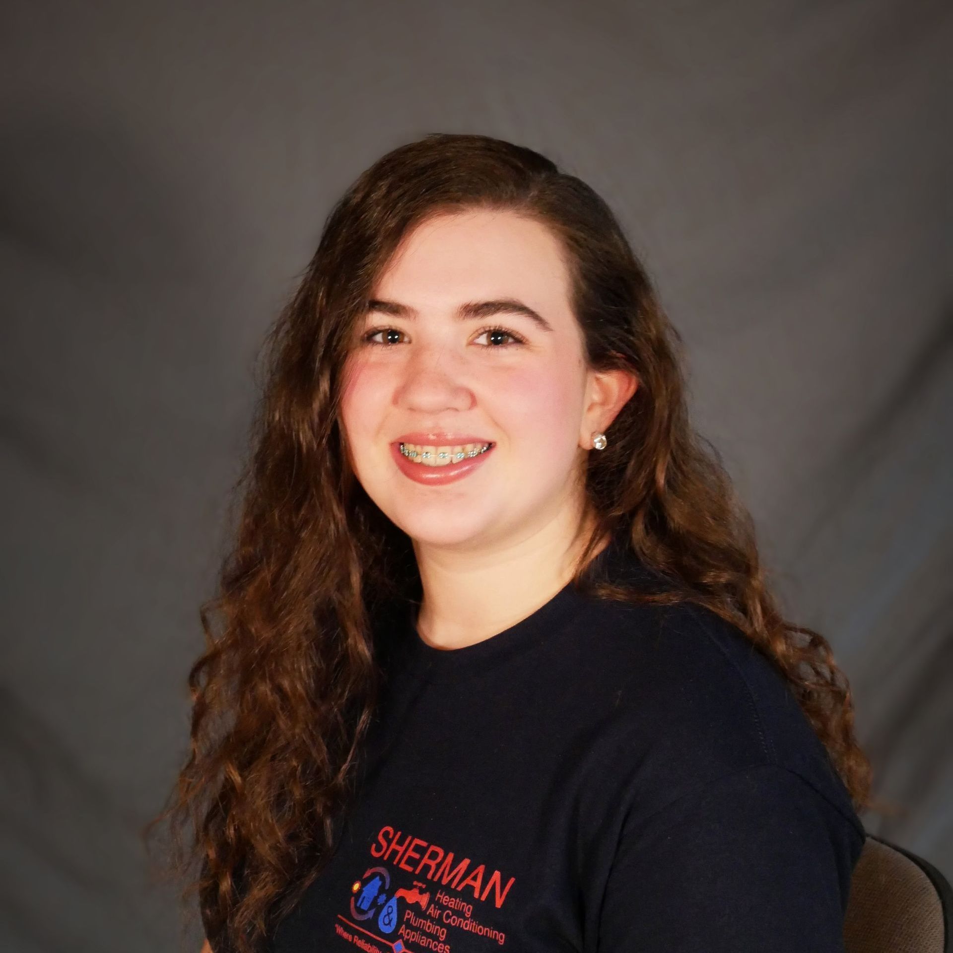 A woman wearing a sherman t-shirt is sitting in a chair.