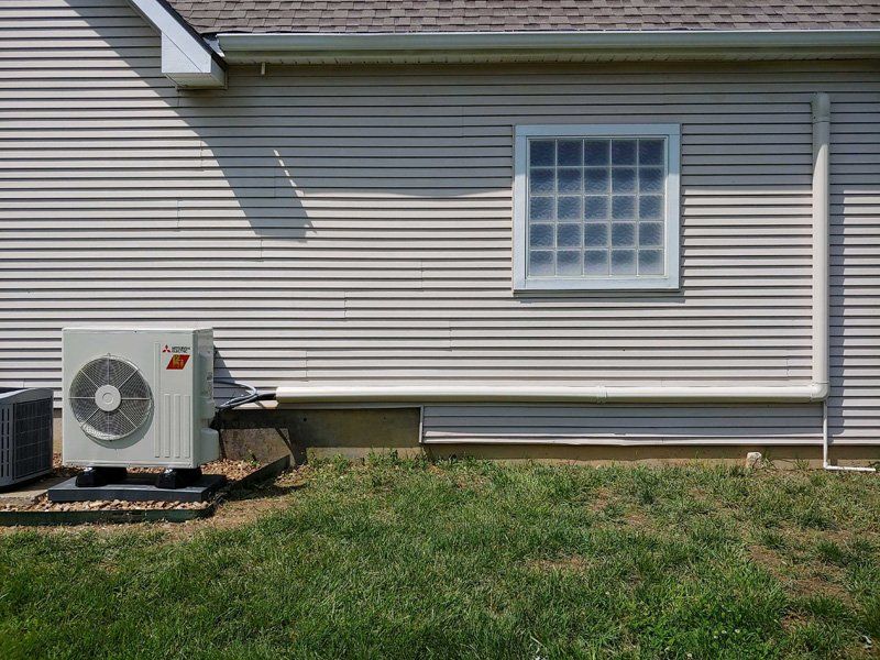 Air conditioning unit outside a light-colored house with a window, white siding, and green grass.