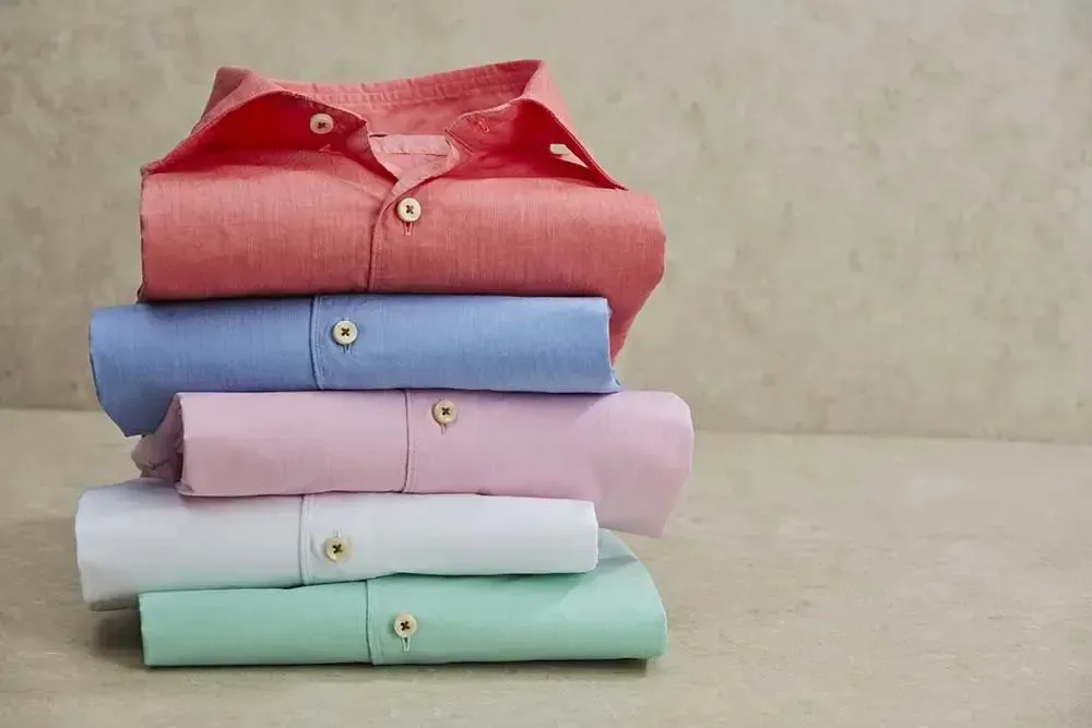 En stak foldede skjorter i forskellige farver på et bord.