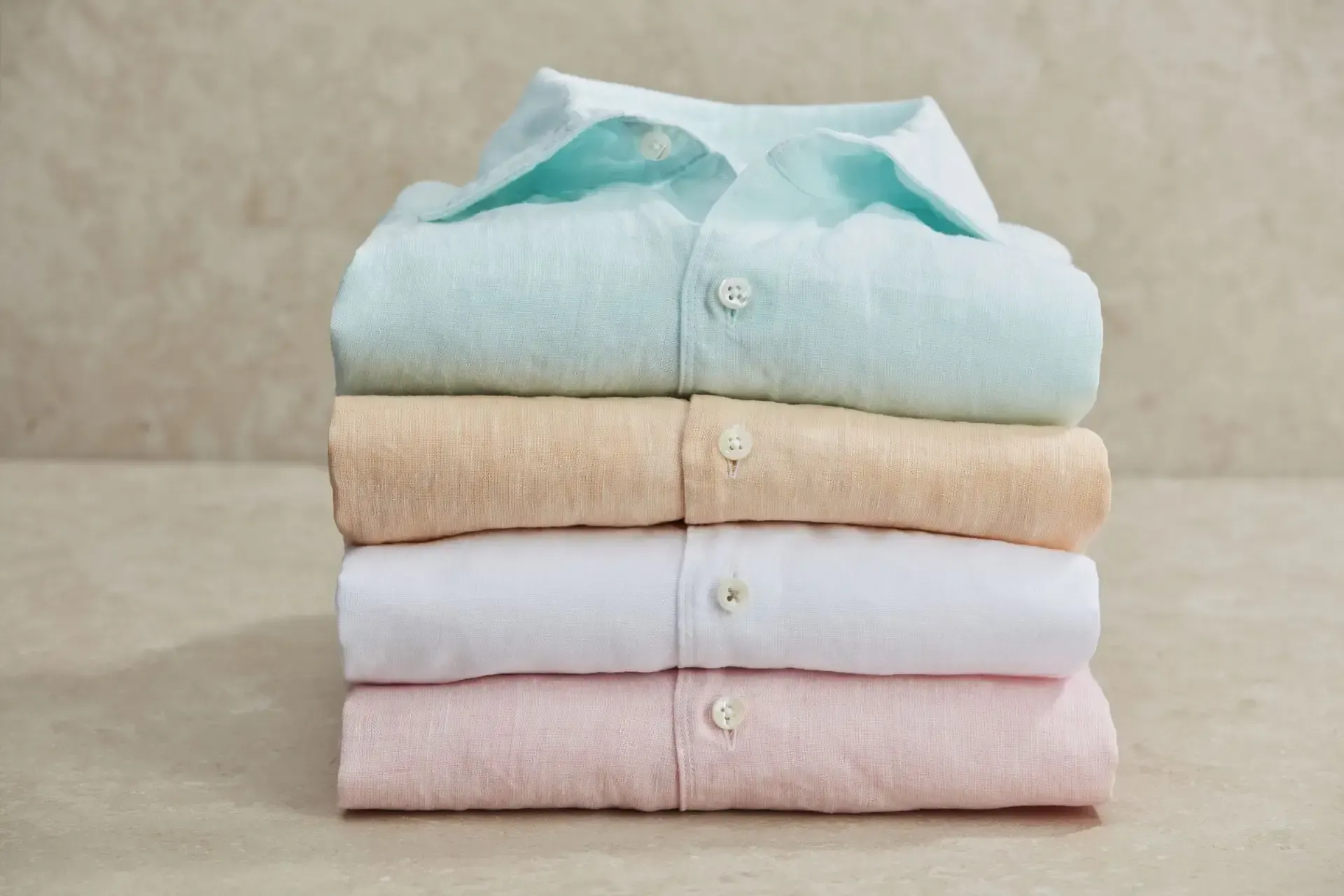 Fire skjorter er stablet oven på hinanden på et bord.