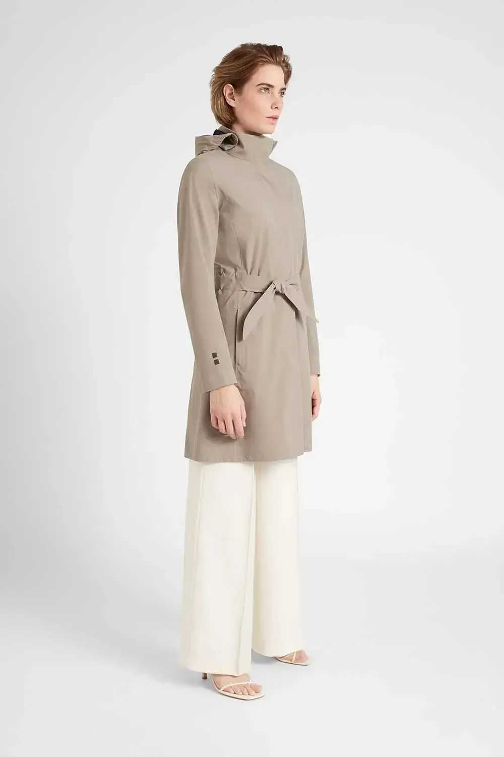 En kvinde er iført en trenchcoat og hvide bukser.