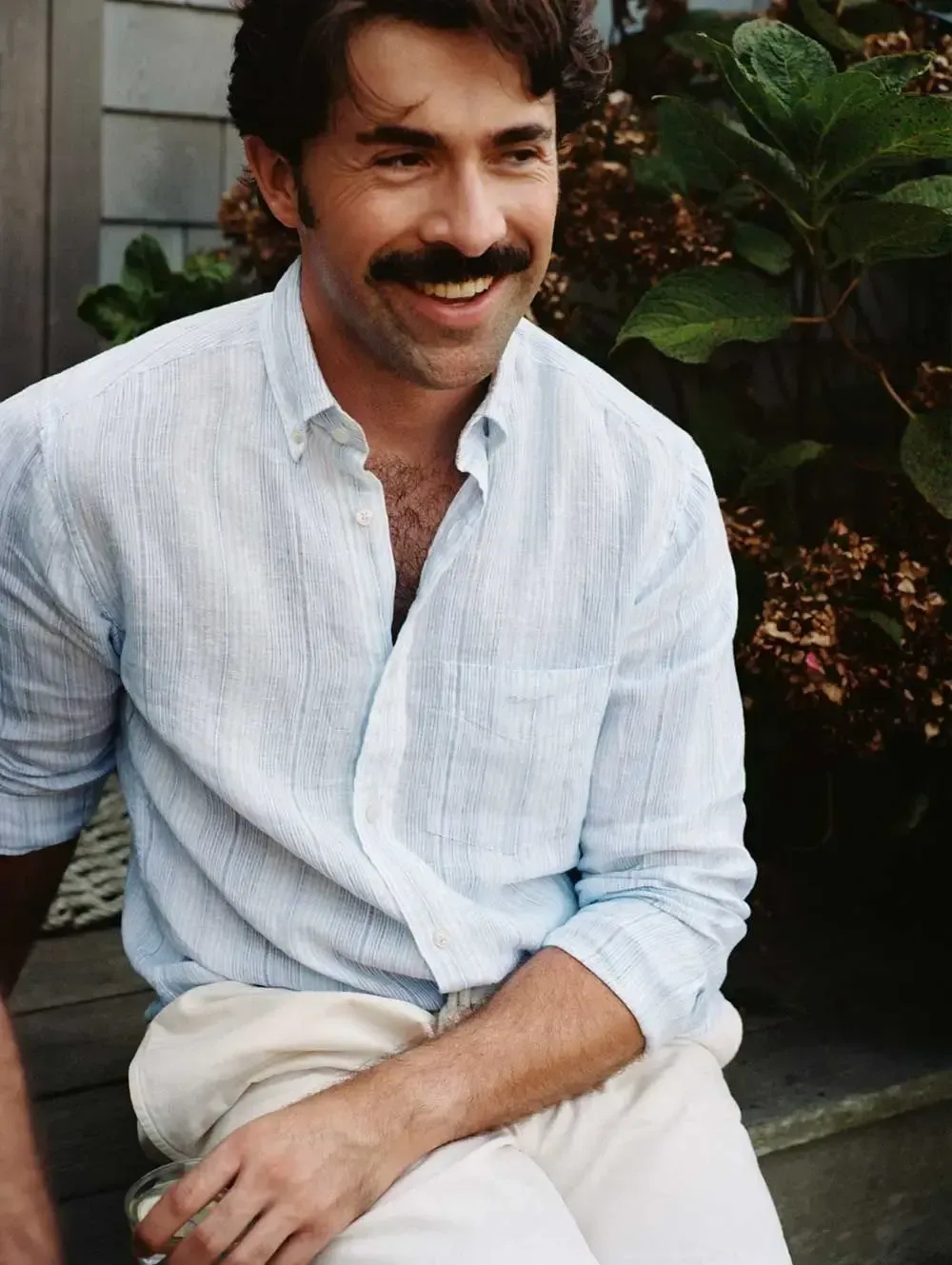 En mand med overskæg har en hvid skjorte og hvide bukser på.