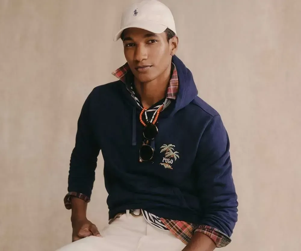 En mand iført en blå hættetrøje og en hvid kasket sidder ned.