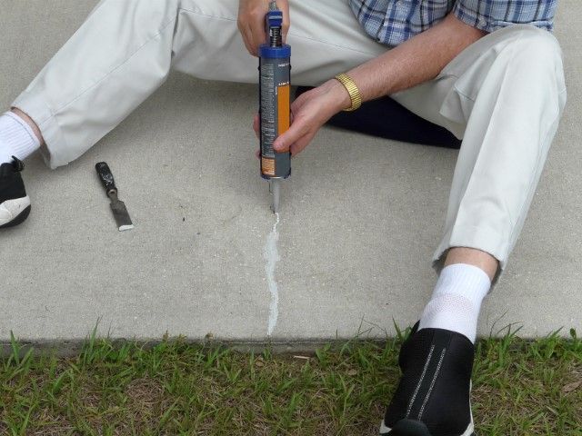 Person using a caulk gun to seal a crack in a concrete step outdoors