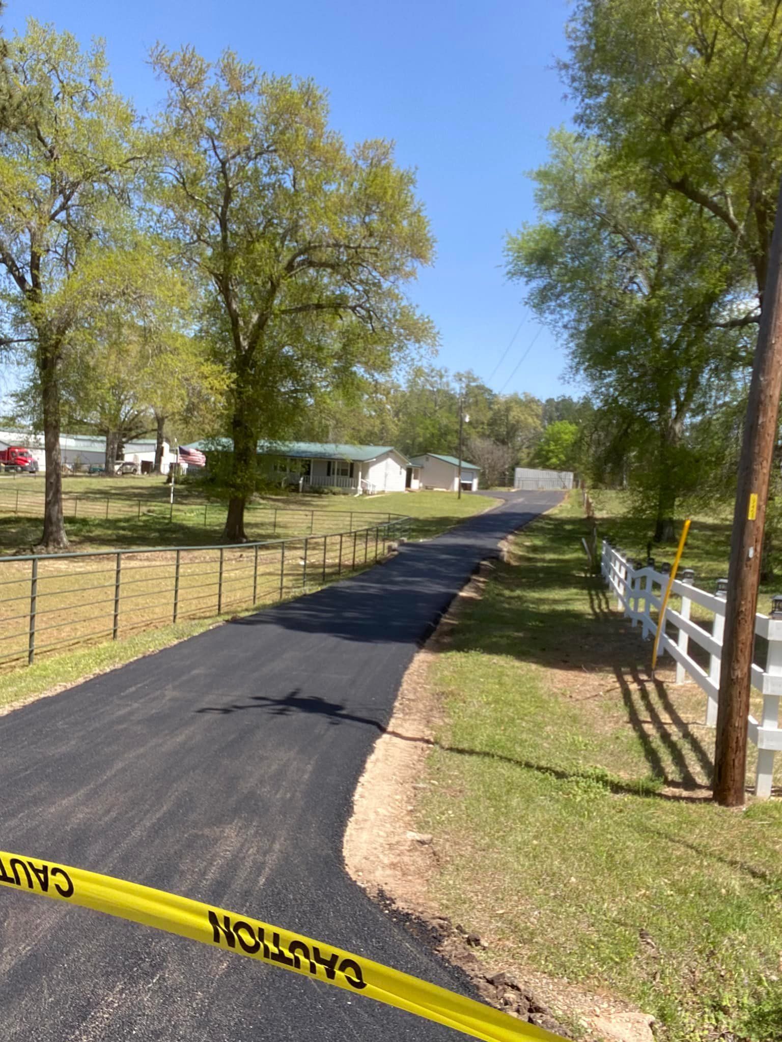 Freshly paved asphalt road leading to a house, yellow caution tape across the bottom.