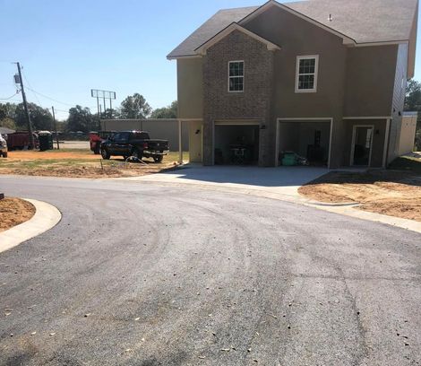 Newly paved driveway leads to a two-story house with garages. Construction materials and trucks visible.