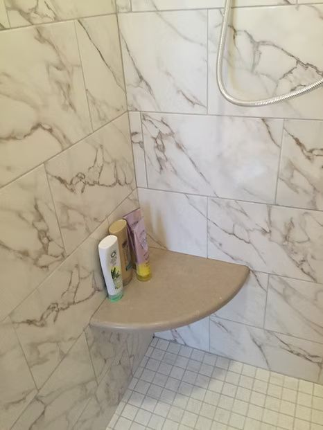 Shower corner with a shelf holding shampoo bottles against marble-look tile.