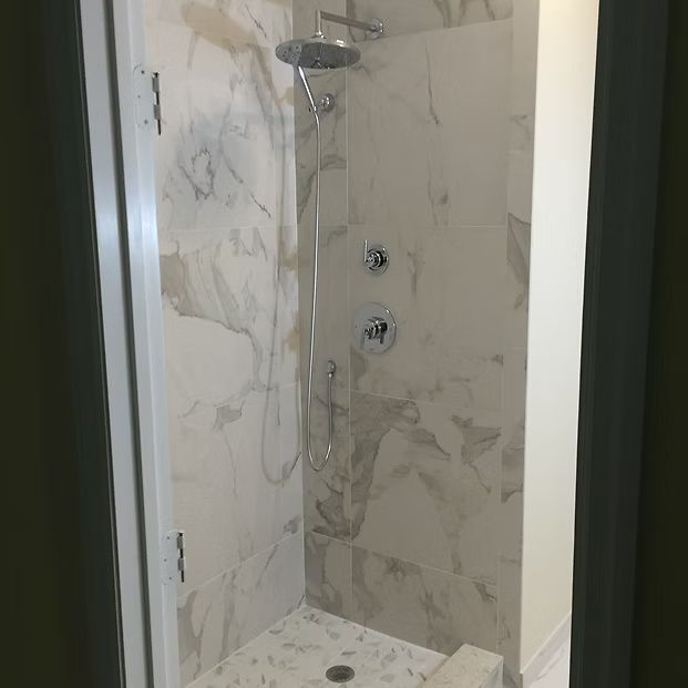 Marble-tiled shower with a rainfall showerhead, handheld sprayer, and built-in bench.