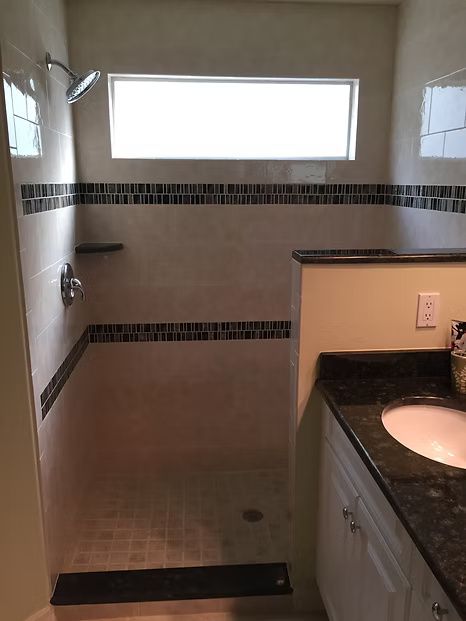 Bathroom with walk-in shower, beige walls, mosaic tile accent, rectangular window, and vanity with dark countertop.