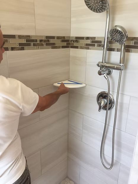 Person installing a shower shelf in a tiled shower.