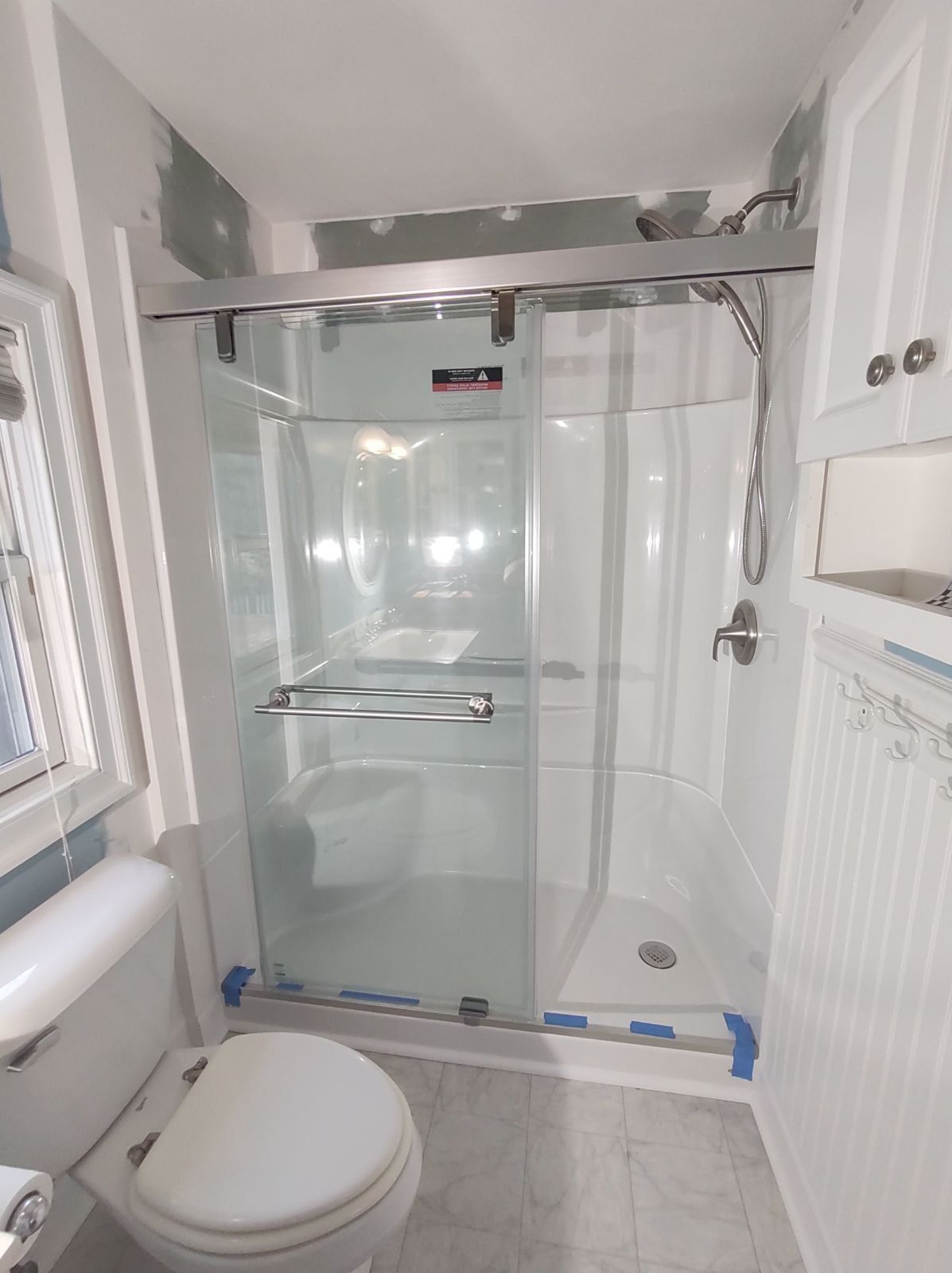Bathroom with glass shower, toilet, and white cabinets.