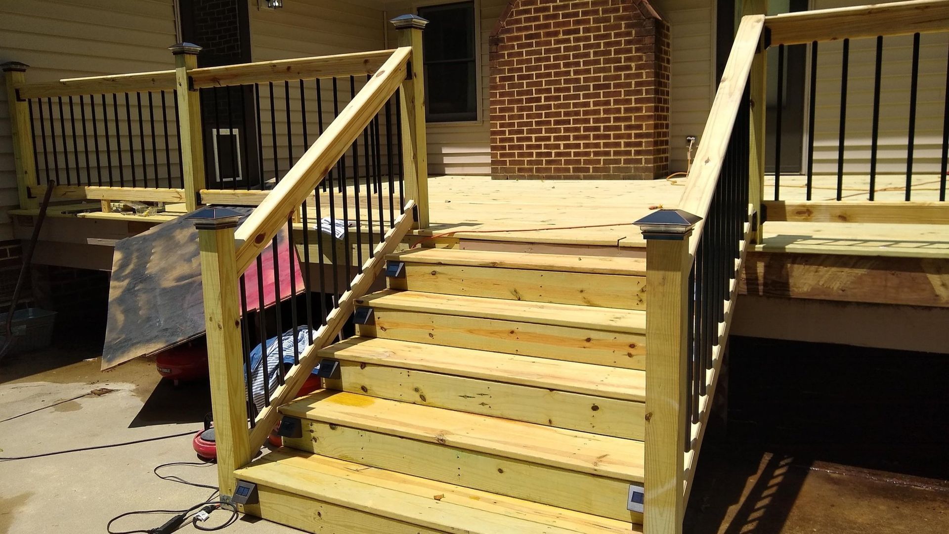 Wooden deck with steps and black railings leading to a brick wall entrance.