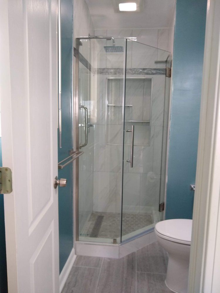 Small bathroom with a glass shower, white toilet, and teal walls.
