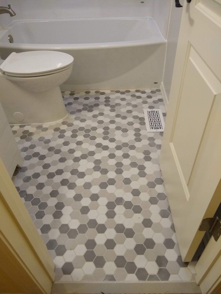 Bathroom with hexagon tile floor in shades of gray, white toilet and tub.