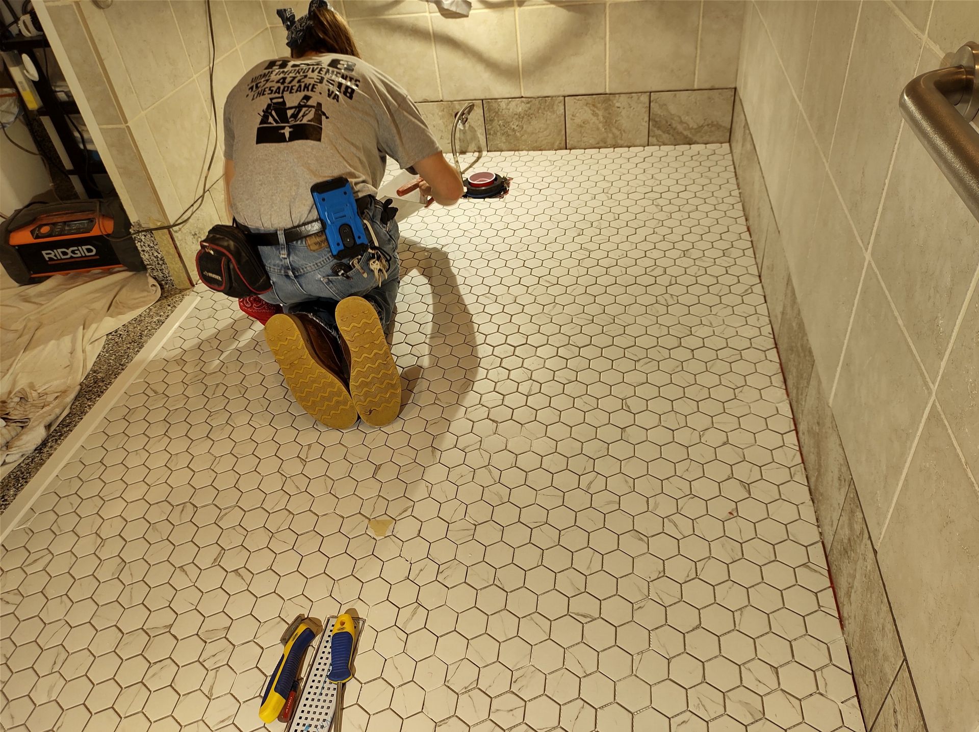 Person tiling a bathroom floor with white honeycomb tiles.