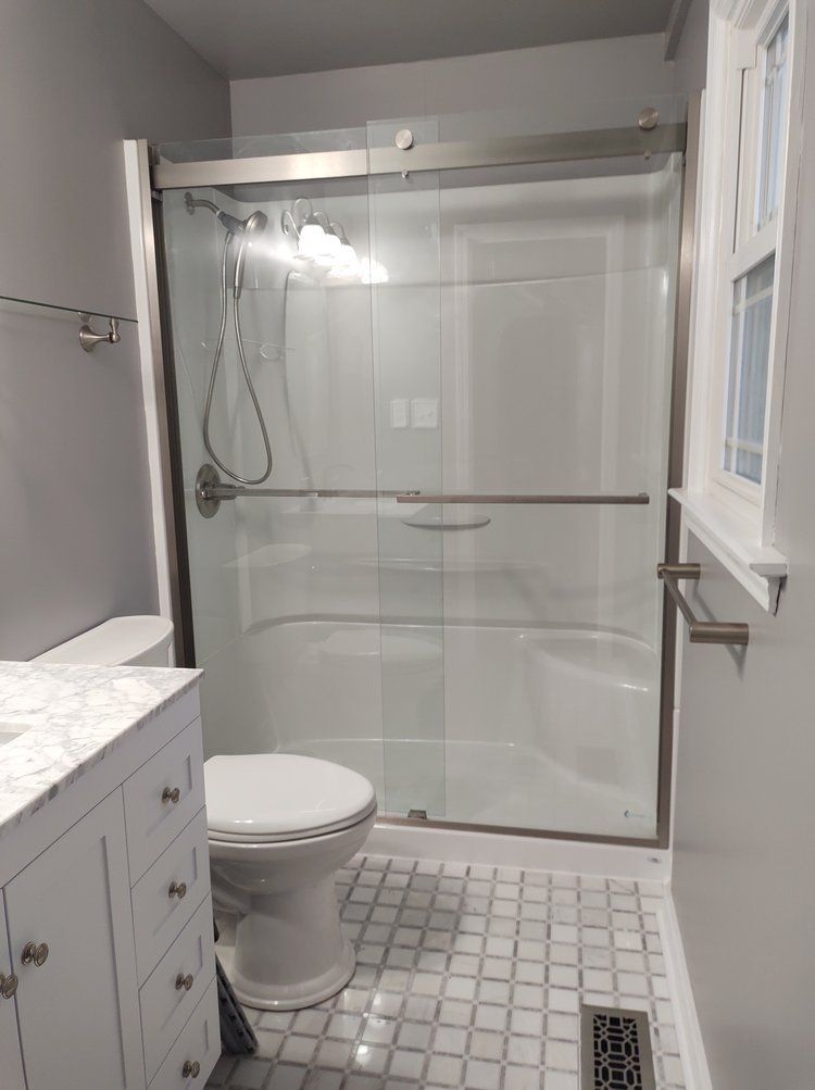 Bathroom with a glass shower, toilet, vanity, and gray and white tiled floor.