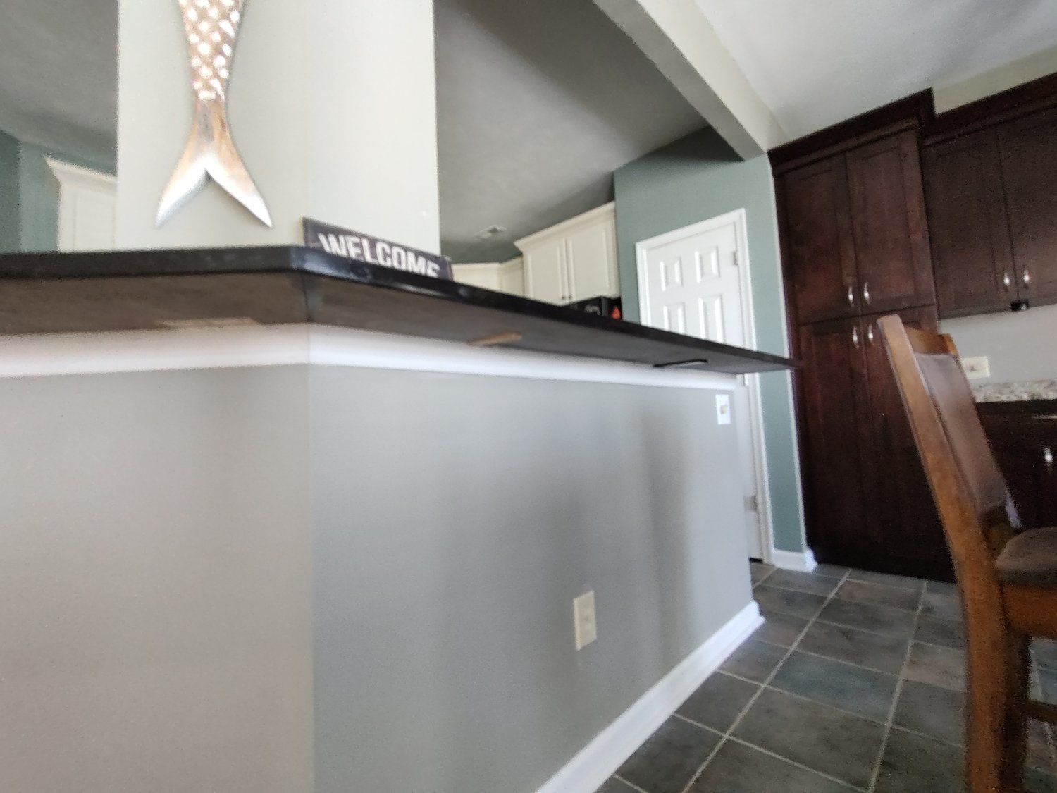 Gray kitchen island with black countertop, dark cabinets, and a welcome sign.
