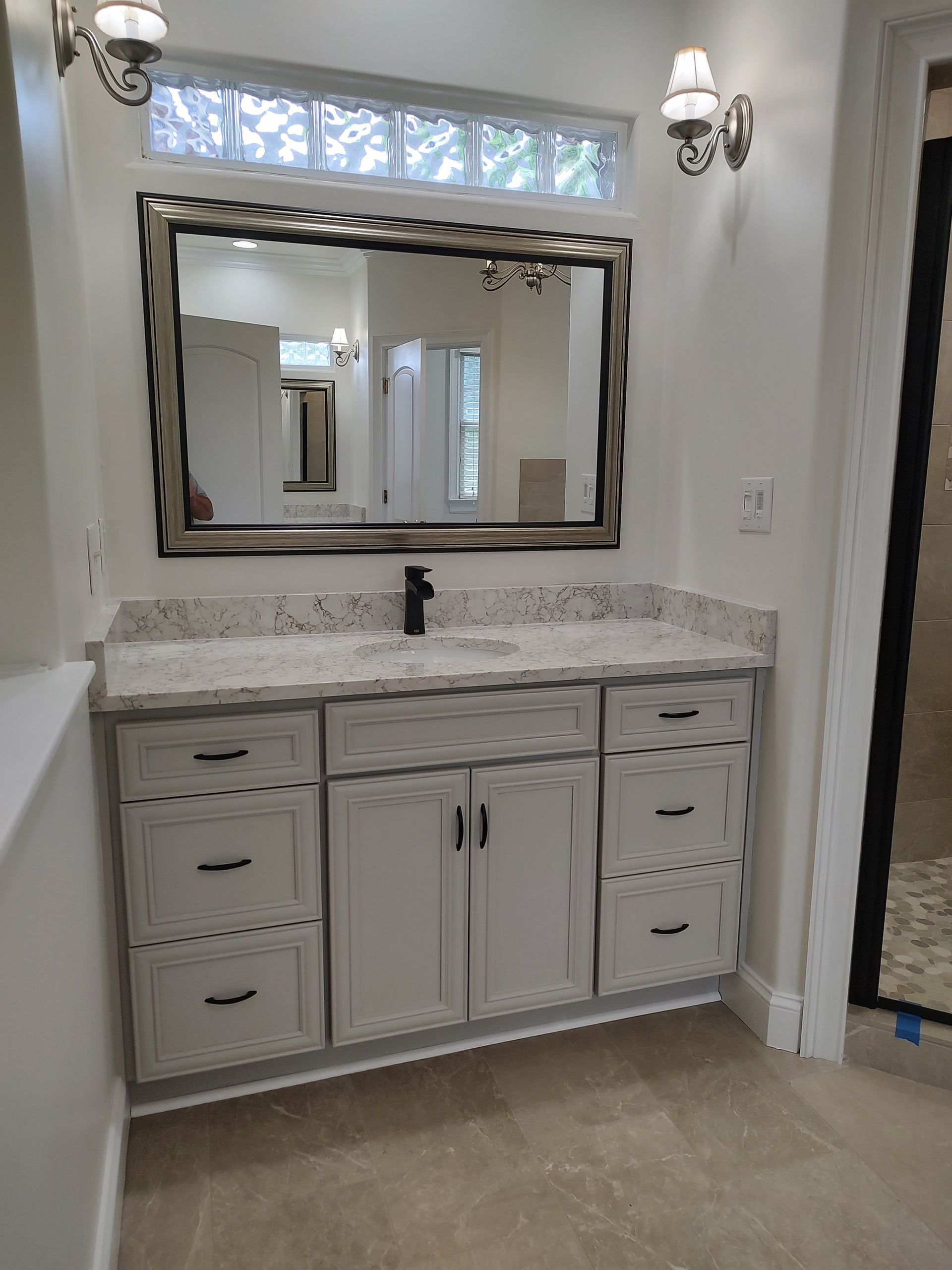 Bathroom vanity with white cabinets, granite countertop, large mirror, and black faucet.