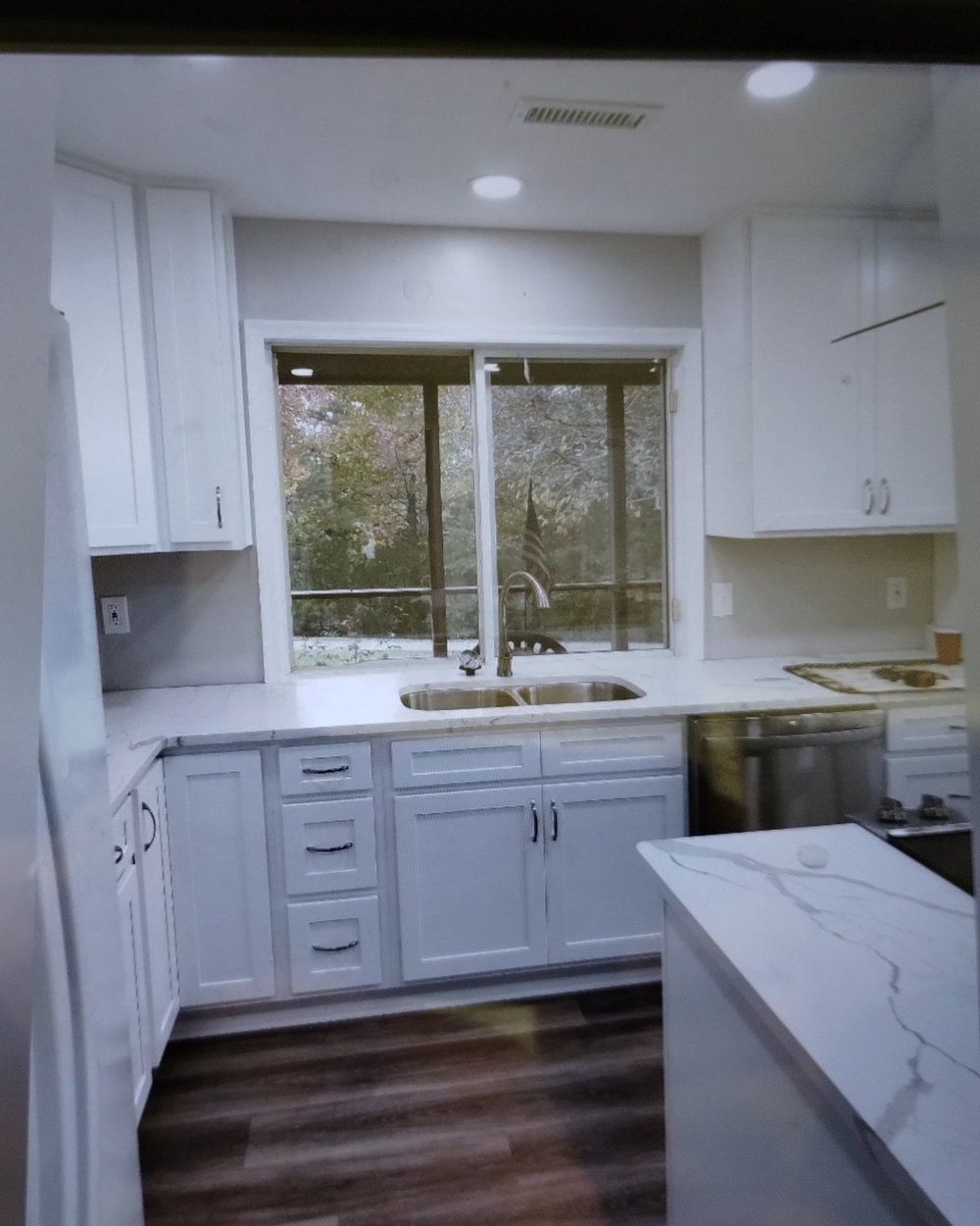 White kitchen with cabinets, countertops, and a window overlooking trees.