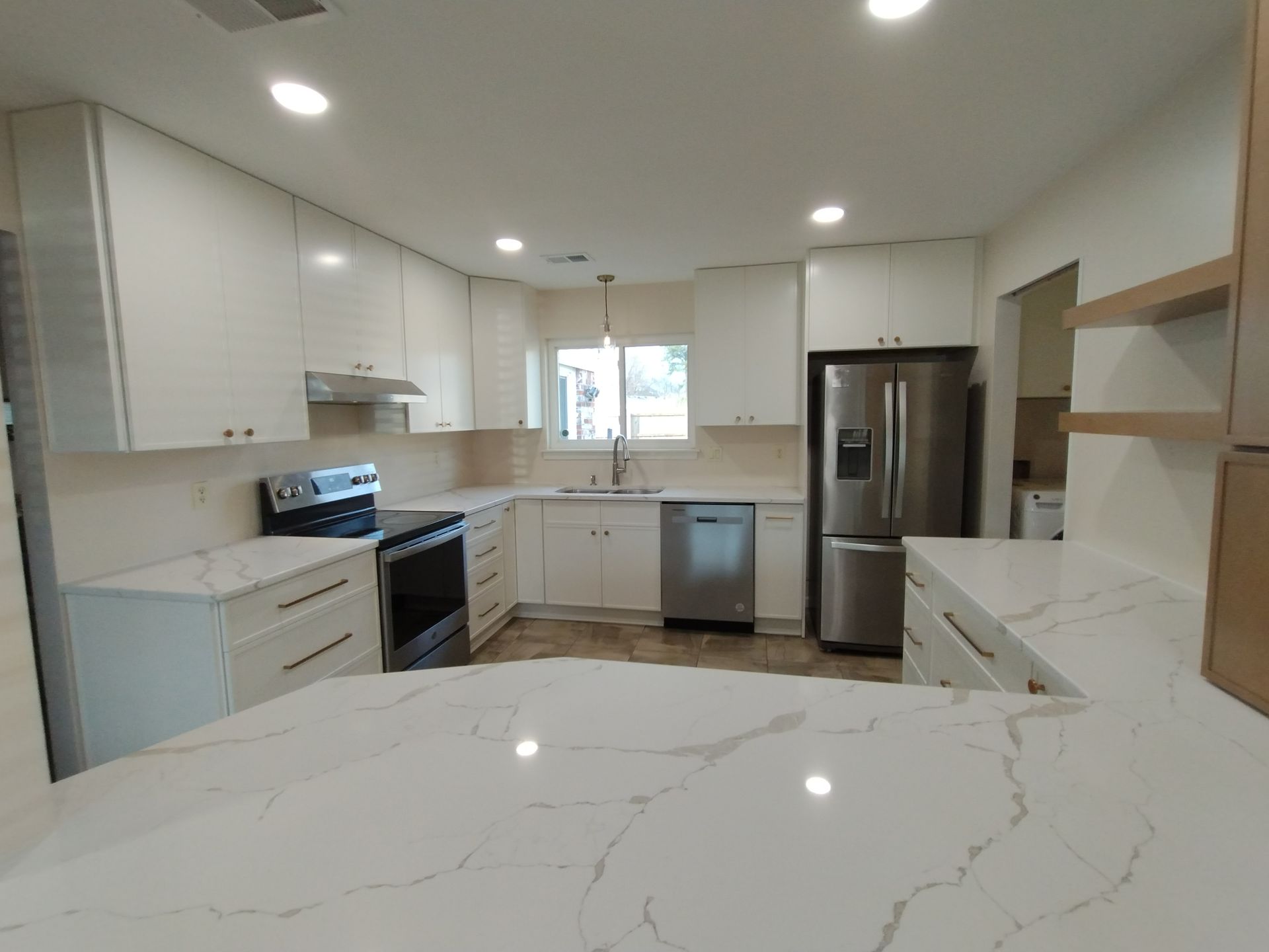 Modern white kitchen with marble countertops, stainless steel appliances, and overhead cabinets.