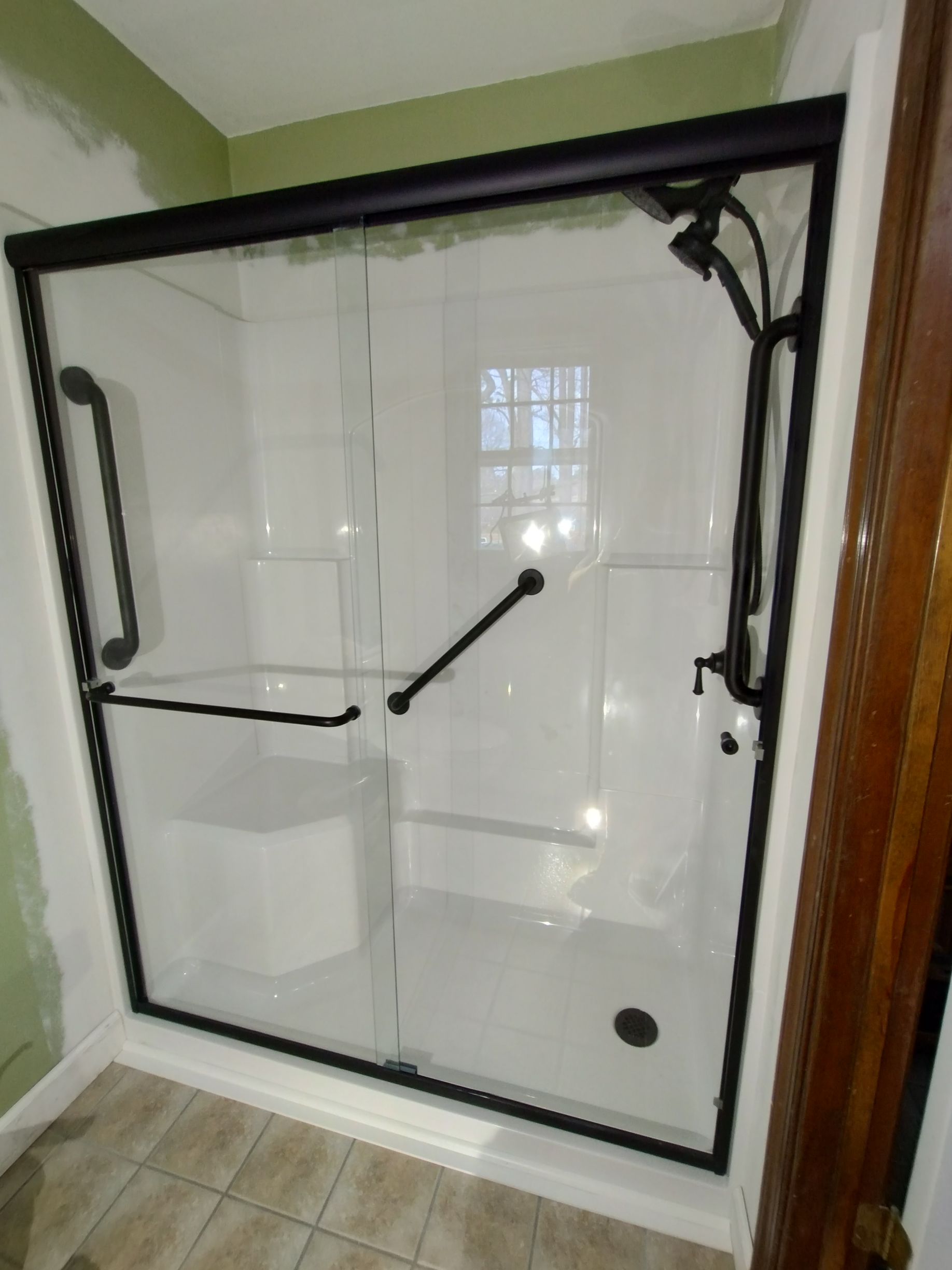 Black-framed glass shower with grab bars, white walls, and a tiled floor.