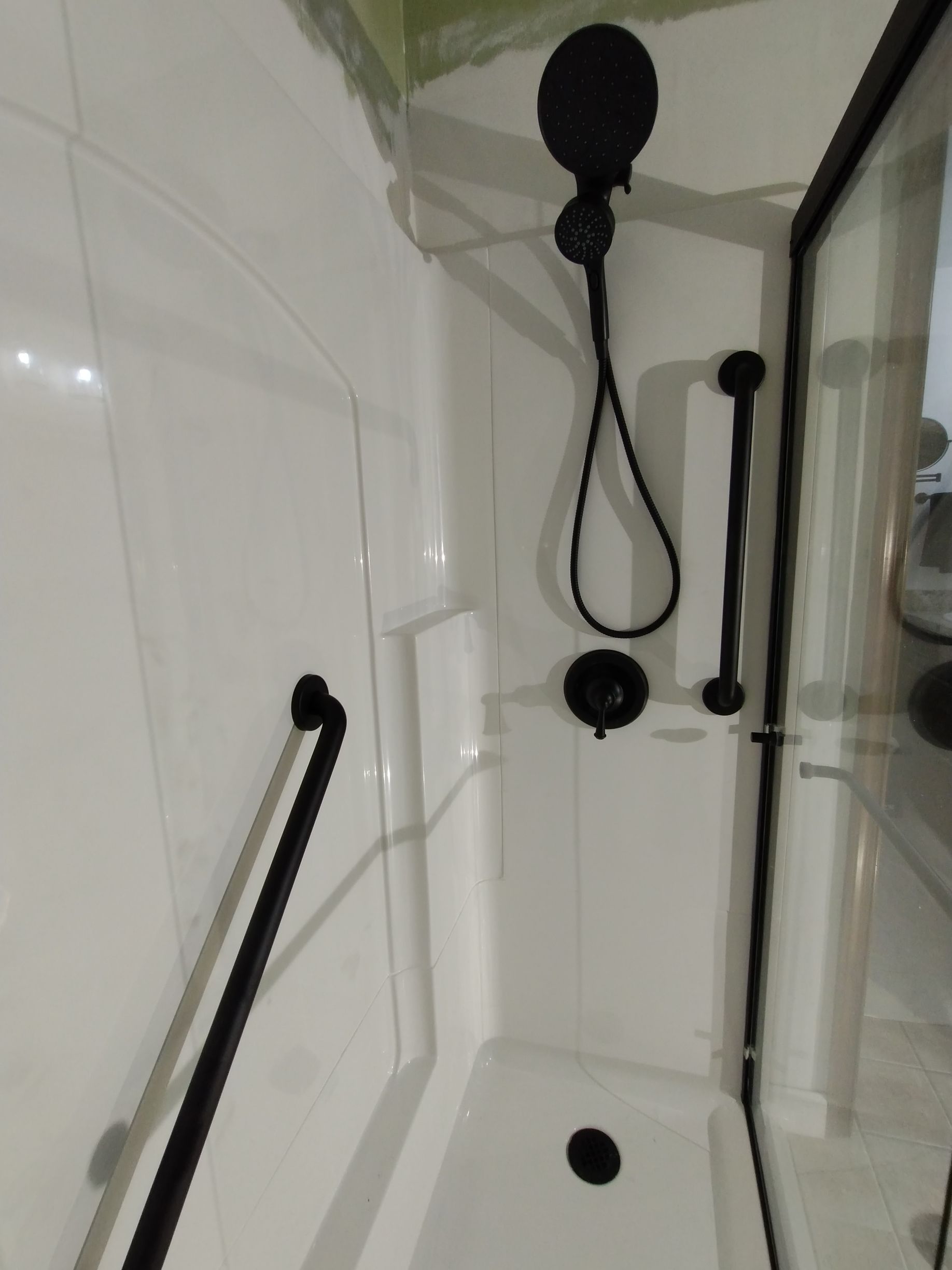 Black and white shower stall with handrails and shower fixtures; accessible design.