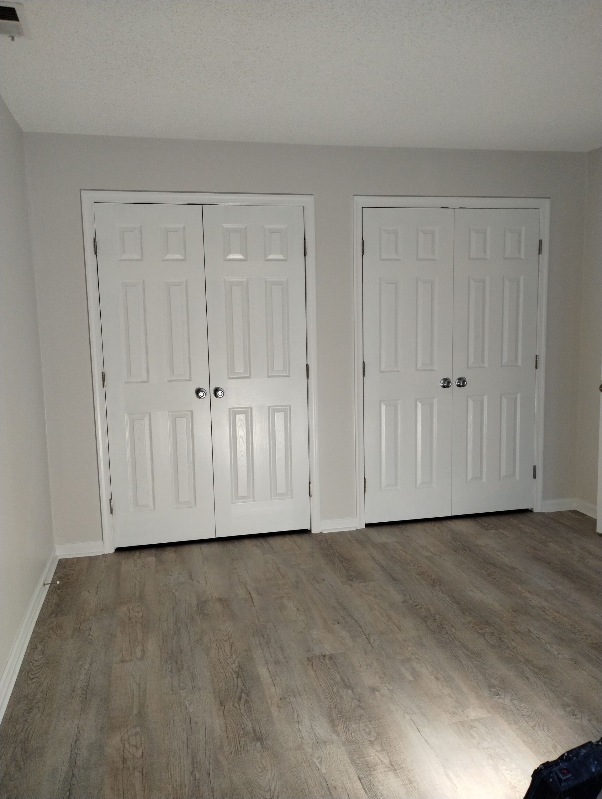 Two white closet doors in a room with wood-look flooring and light gray walls.