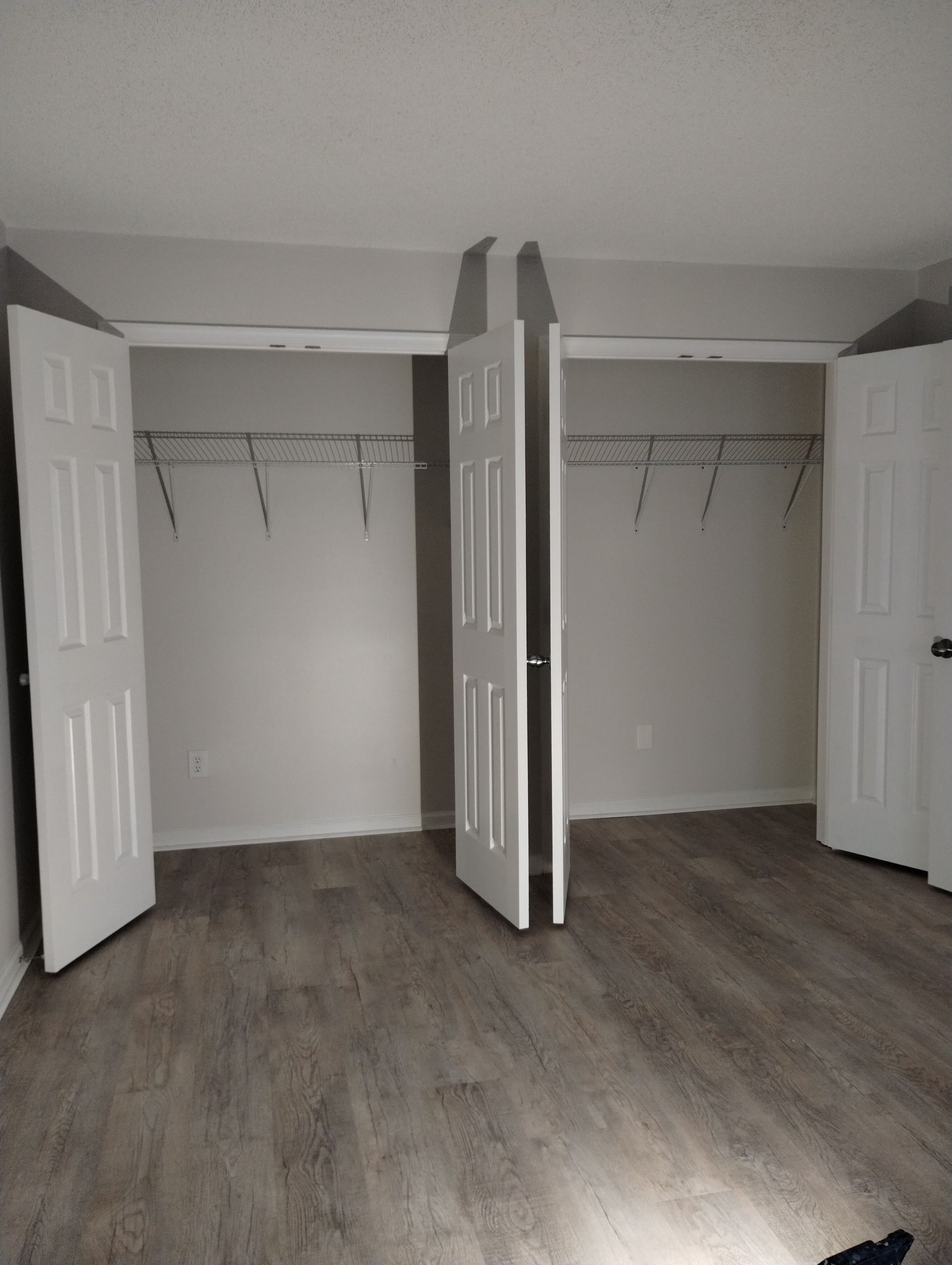 A room with two closets and white doors. Gray wood-look flooring and neutral walls.