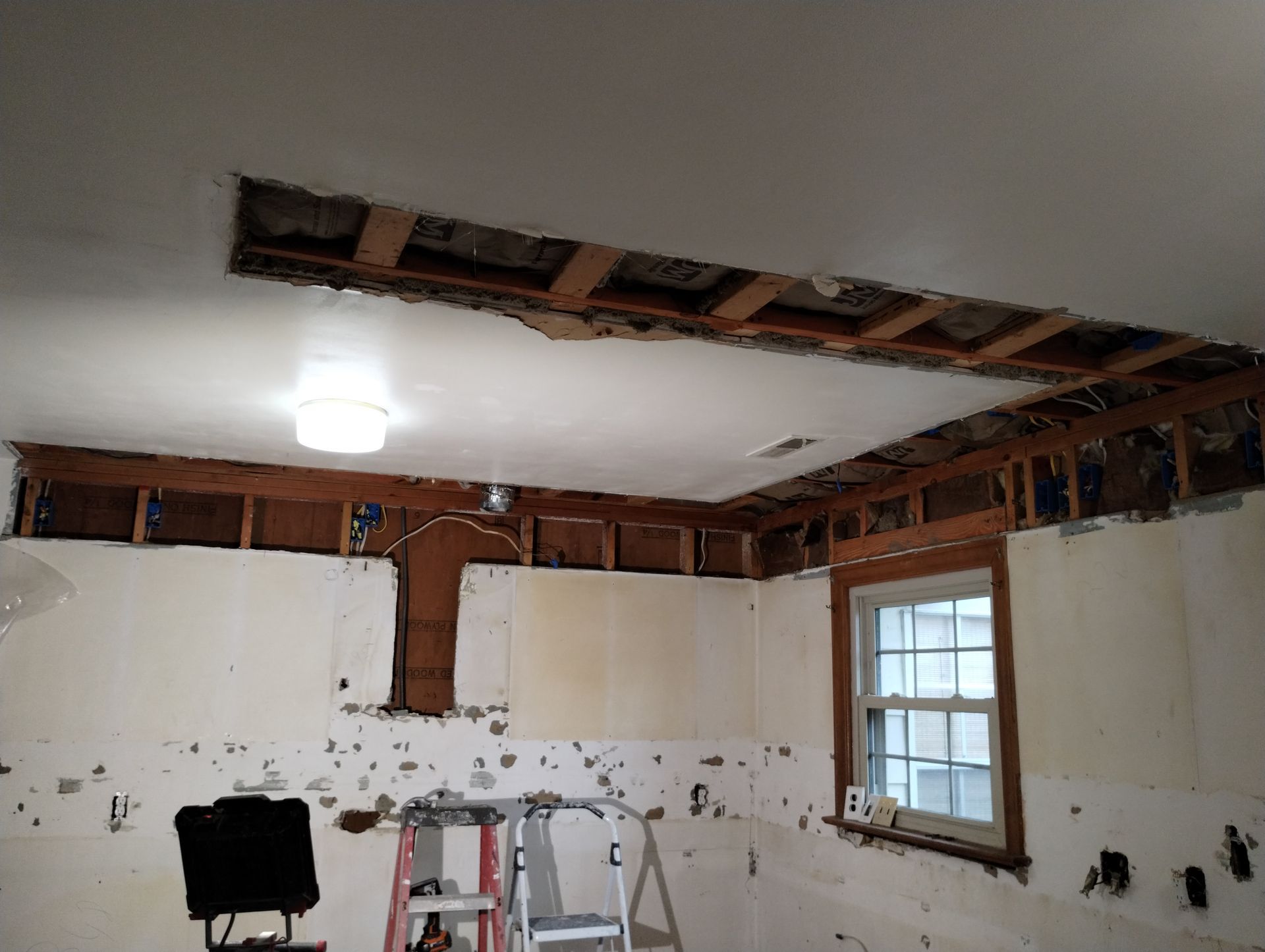 Room under renovation with exposed ceiling joists, damaged drywall, and a window.