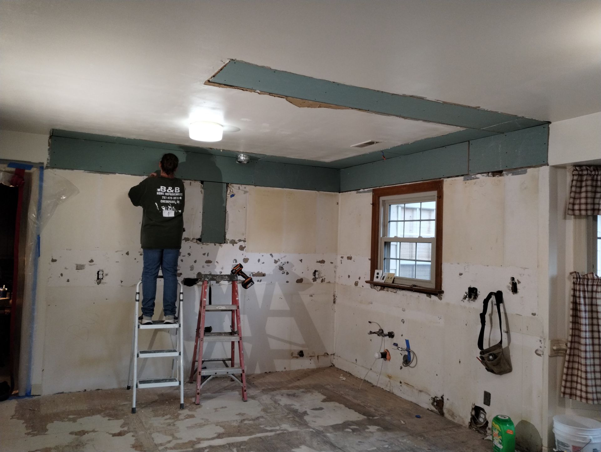 Person on a ladder working on a kitchen ceiling during a renovation.