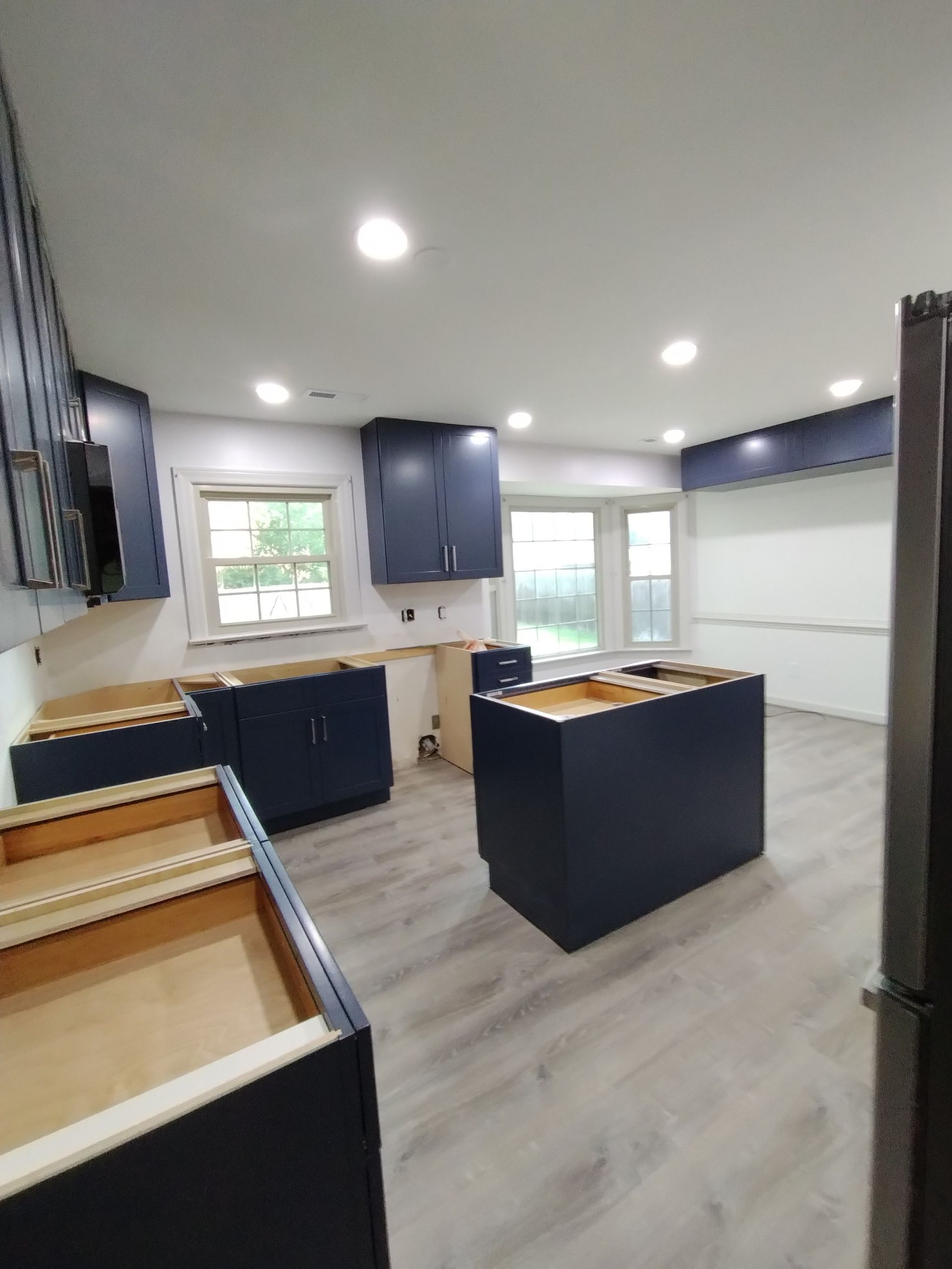 A modern kitchen with navy blue cabinets, a central island, and light-colored flooring.