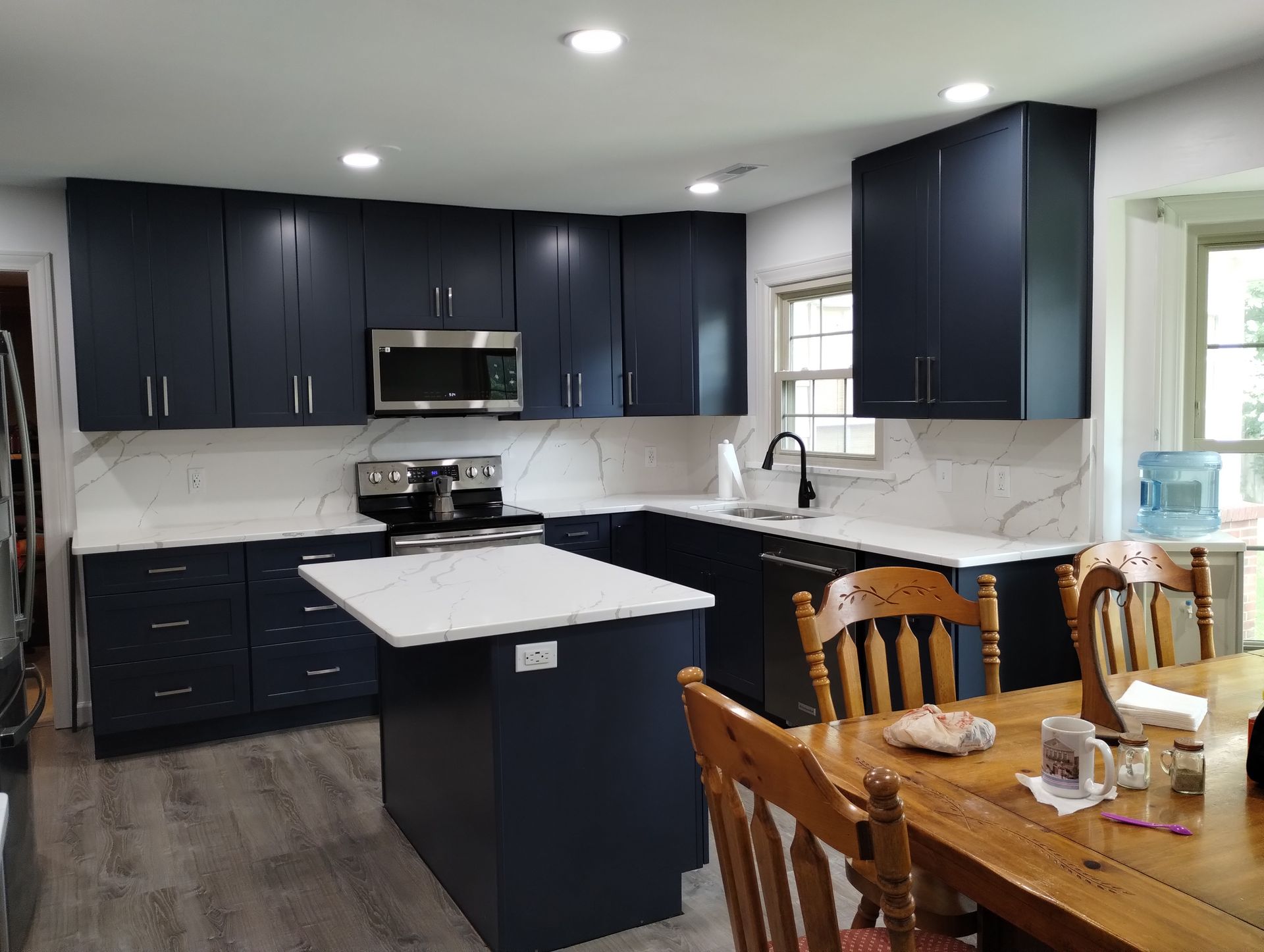 Dark blue kitchen with white countertops, stainless steel appliances, and a wooden table.