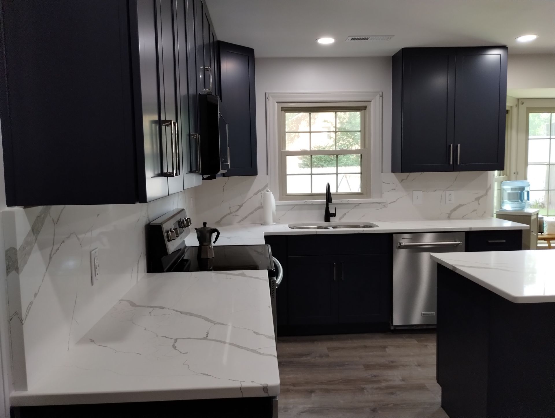Modern kitchen with navy cabinets, white countertops, and stainless steel appliances.