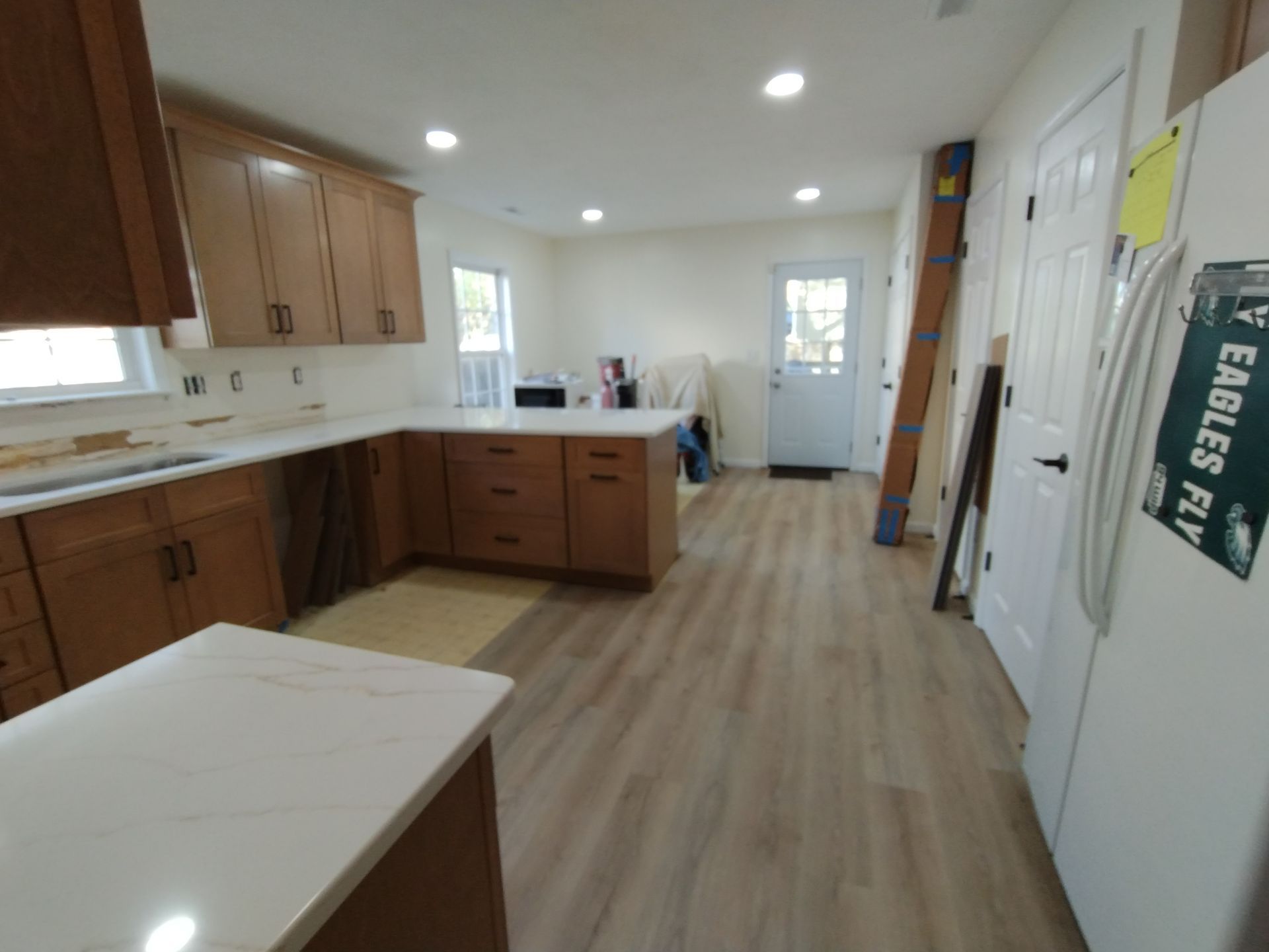 Kitchen undergoing renovation with light wood cabinets, white countertops, and new flooring.